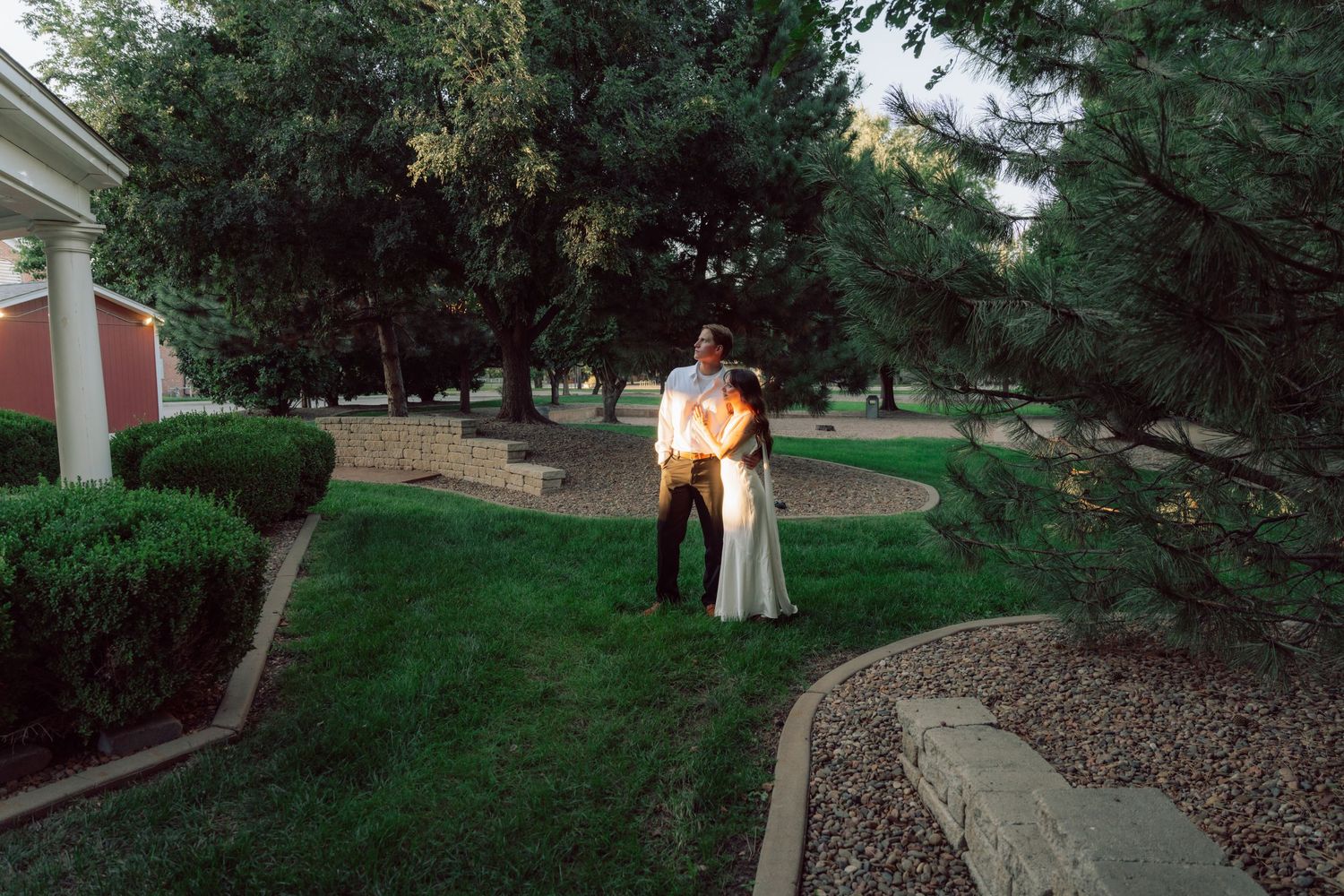 A romantic couple poses together in a garden setting at sunset with glowing golden light.