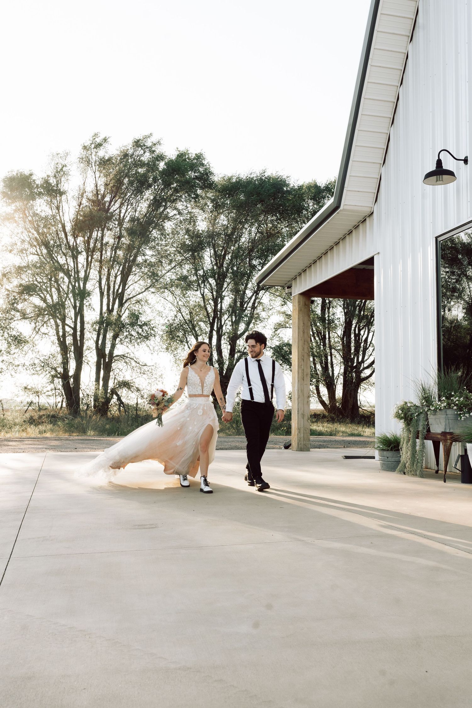 Couple dancing together outside a white barn during sunset.