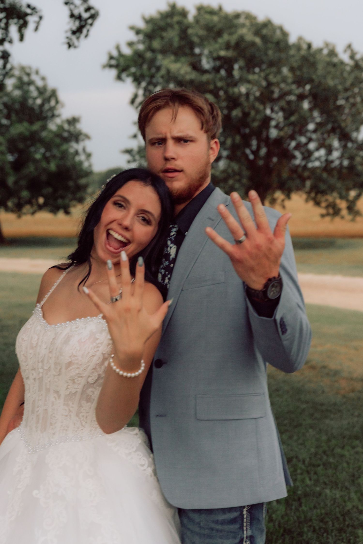 Happy newlyweds showing off wedding rings while embracing outdoors.