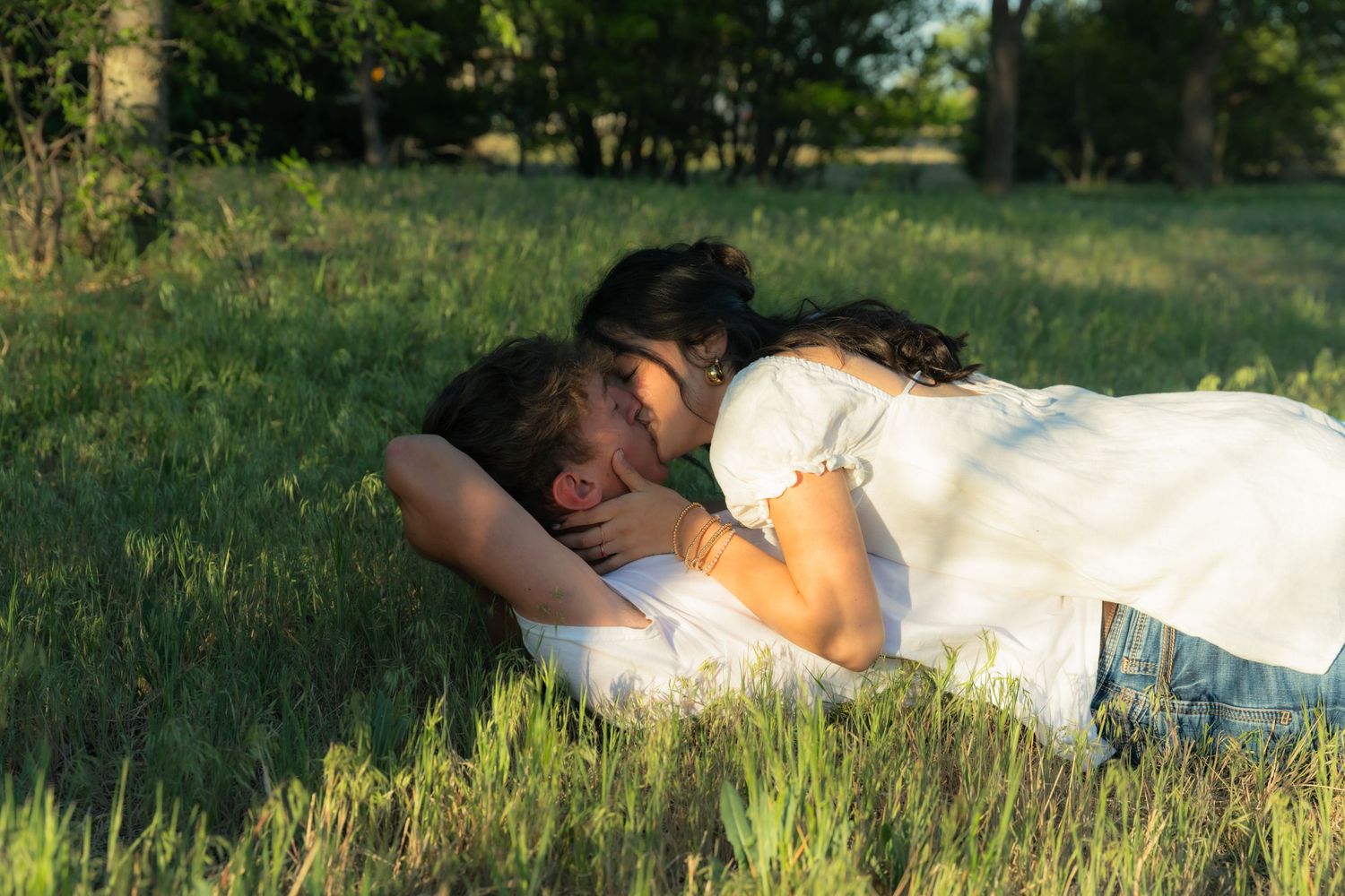 Couple sharing a tender moment lying in lush green grass field on a sunny day.