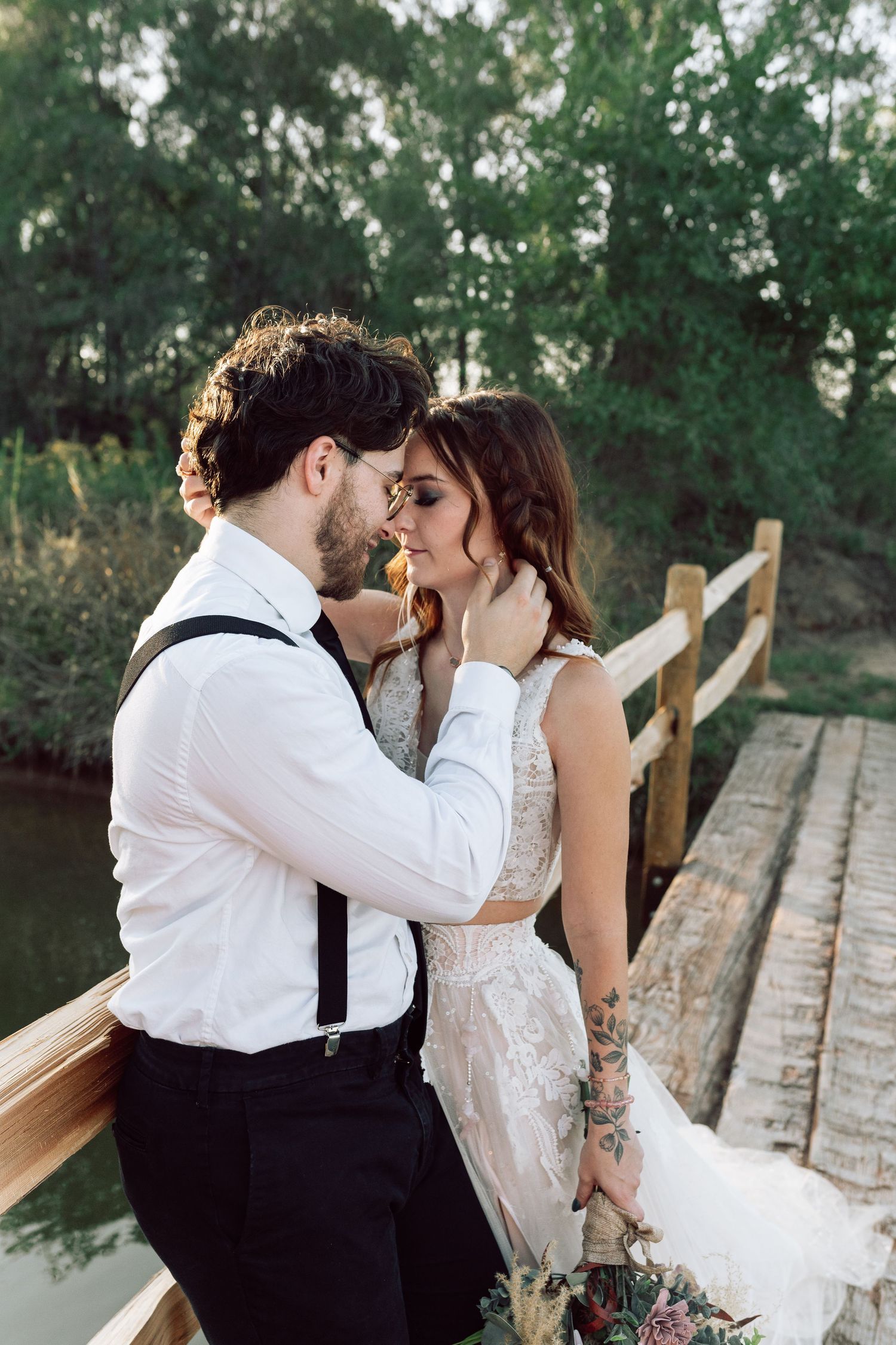 Romantic wedding couple shares tender moment on rustic bridge at sunset.