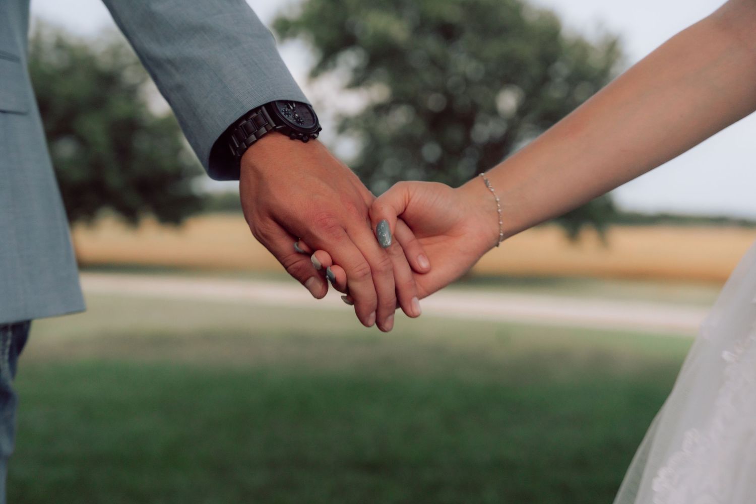 Close-up of newlyweds holding hands in an outdoor wedding setting.
