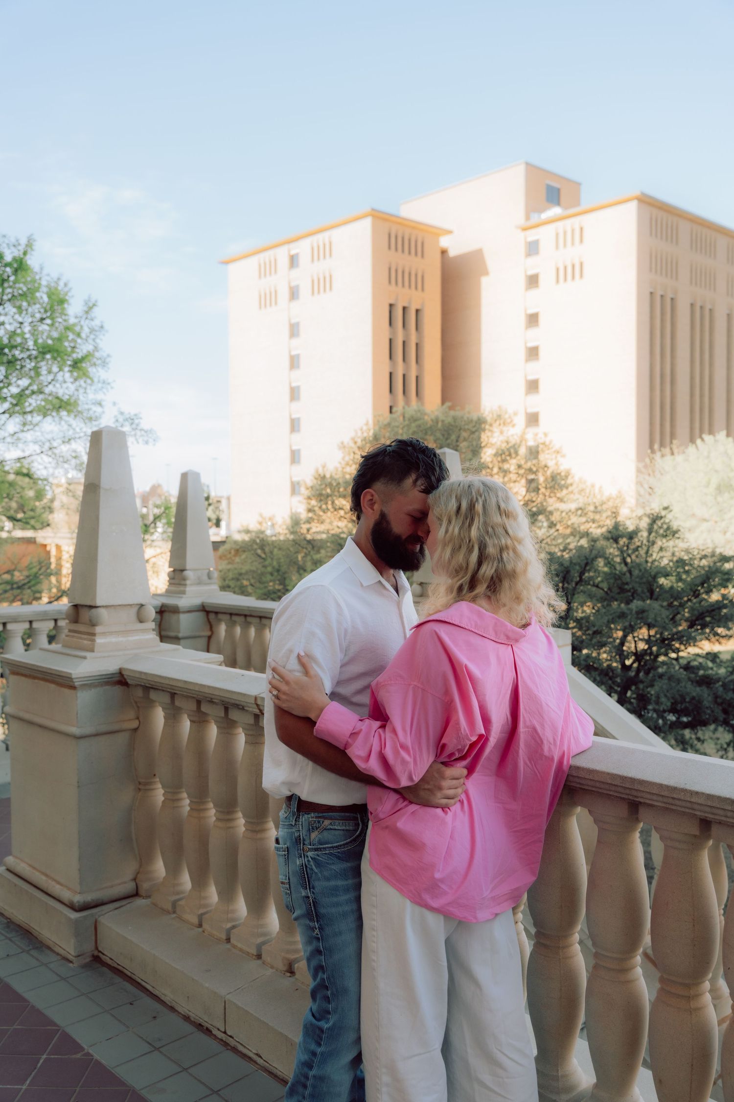 A couple shares an intimate moment on a balcony with a grand building in the background.