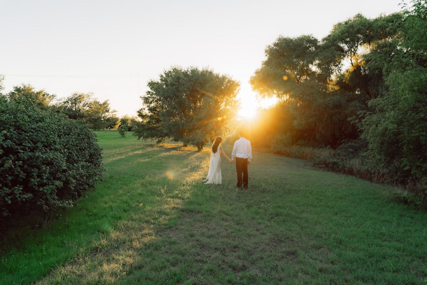 A couple stands together in a serene meadow landscape during a golden sunset.