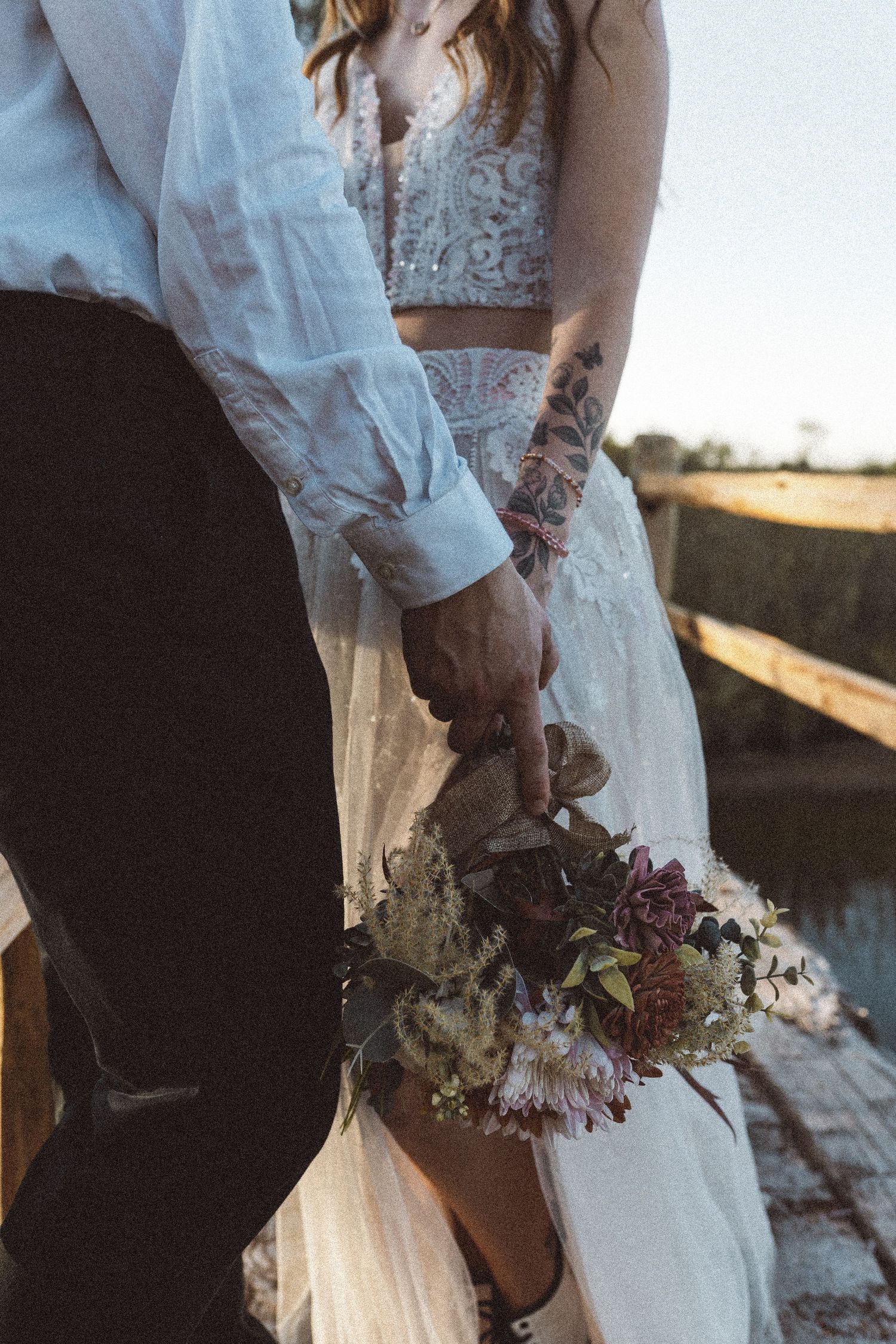 Close-up of couple's hands holding delicate floral bouquet against white dress.