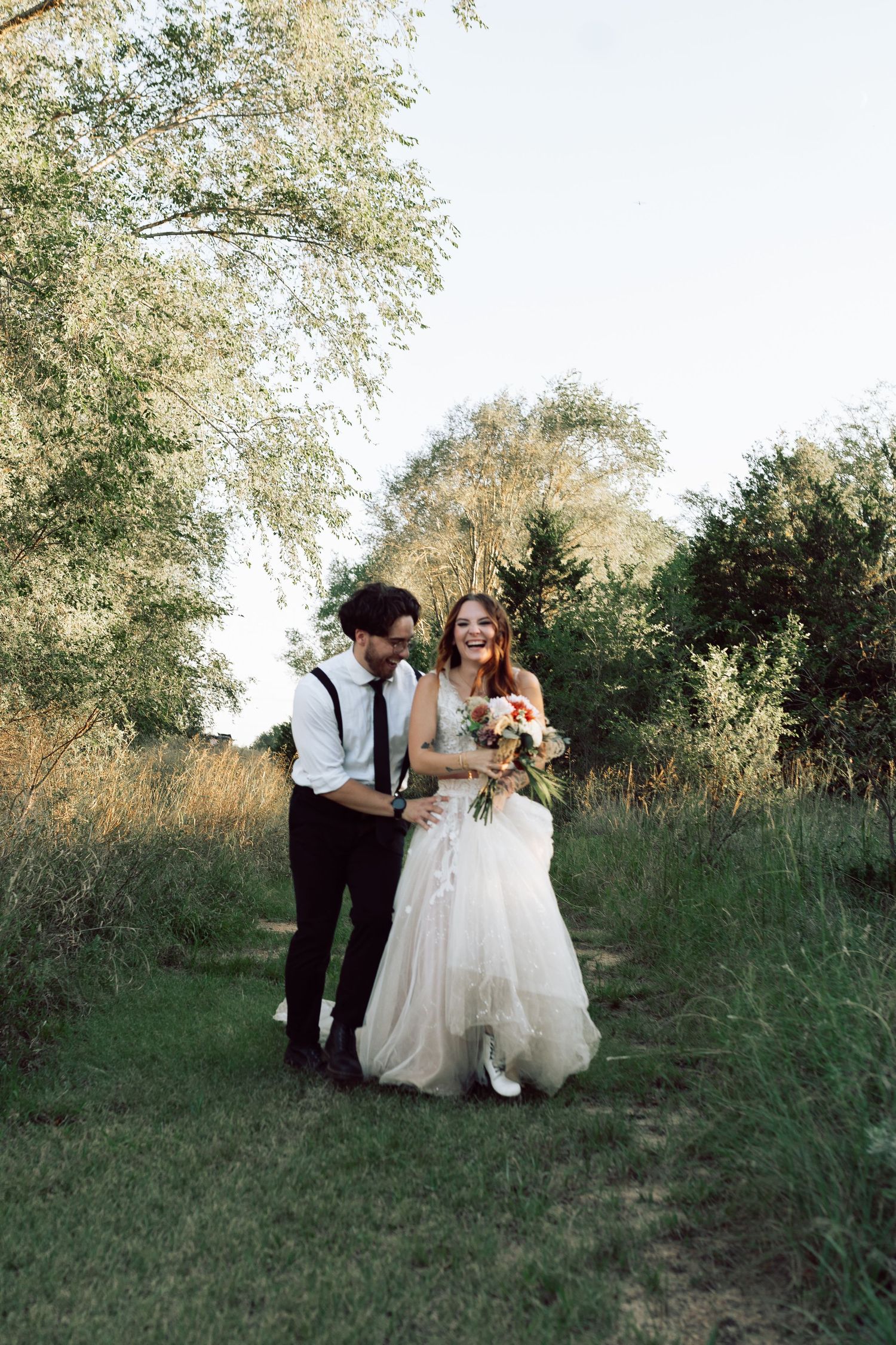 A couple shares a tender moment on a grassy trail surrounded by trees.
