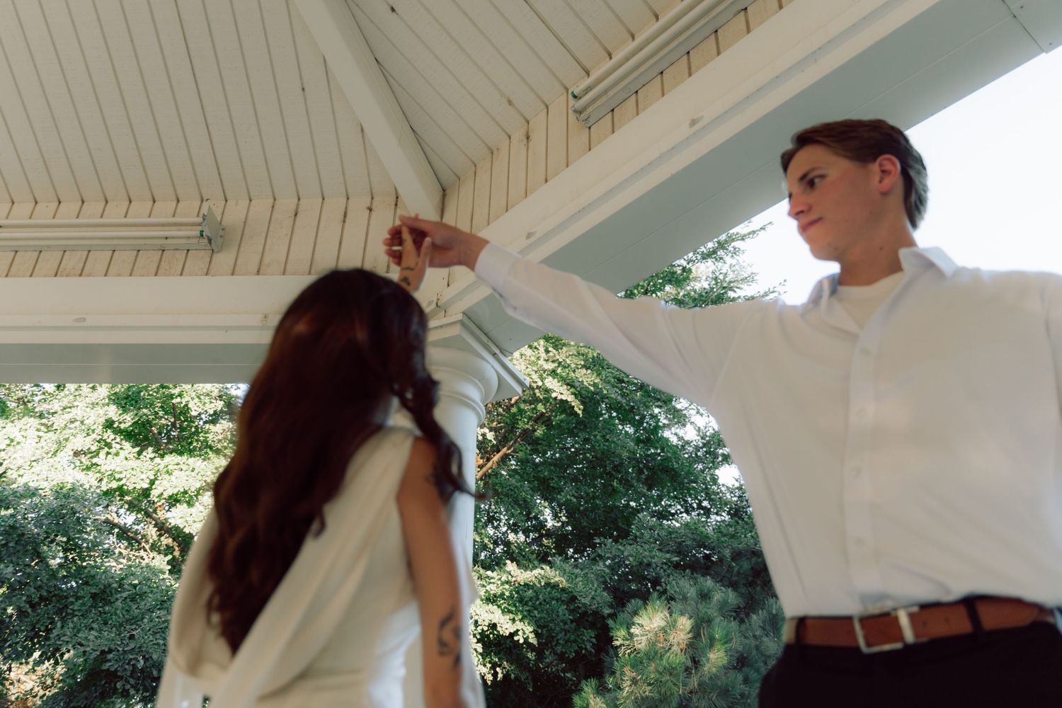 A couple dances together on an elegant white gazebo surrounded by greenery.