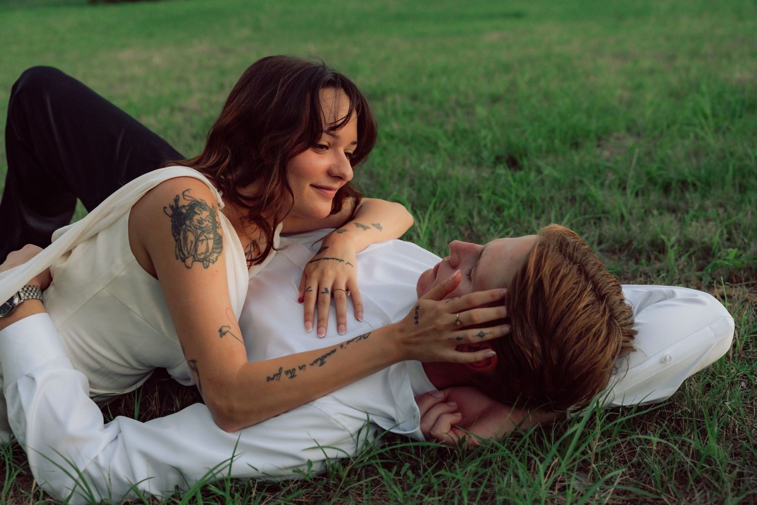 Intimate moment between couple laying in grass during outdoor photo session.