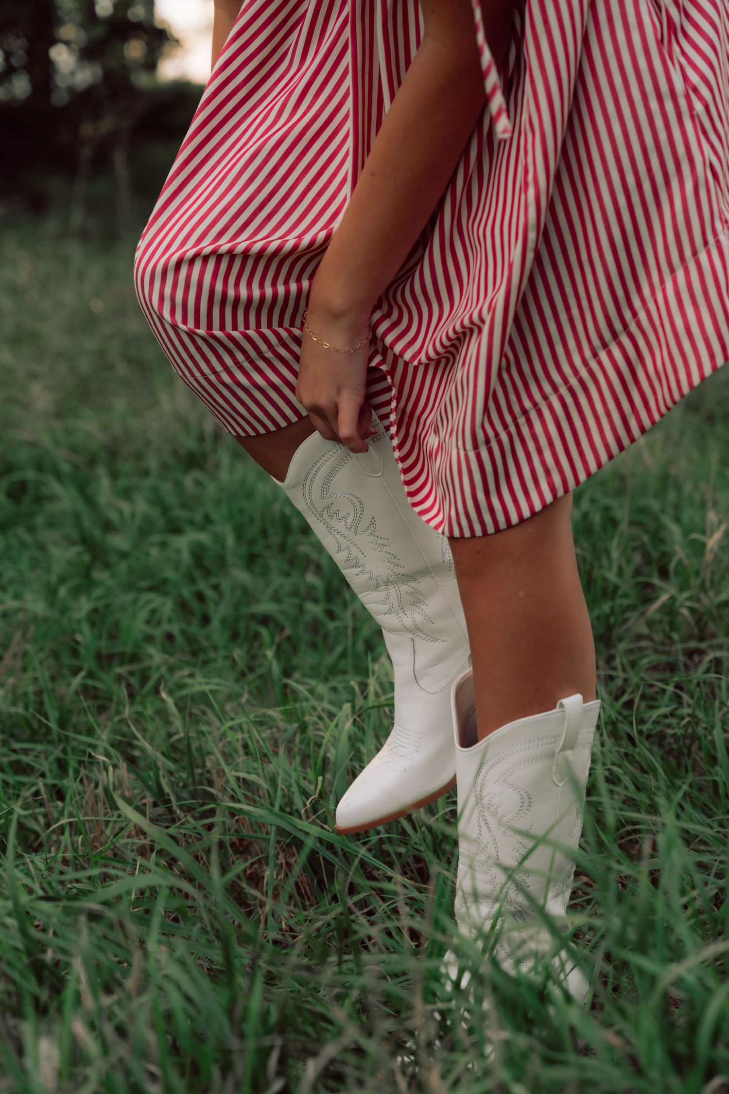 White cowboy boots paired with red and white striped dress against grassy background.