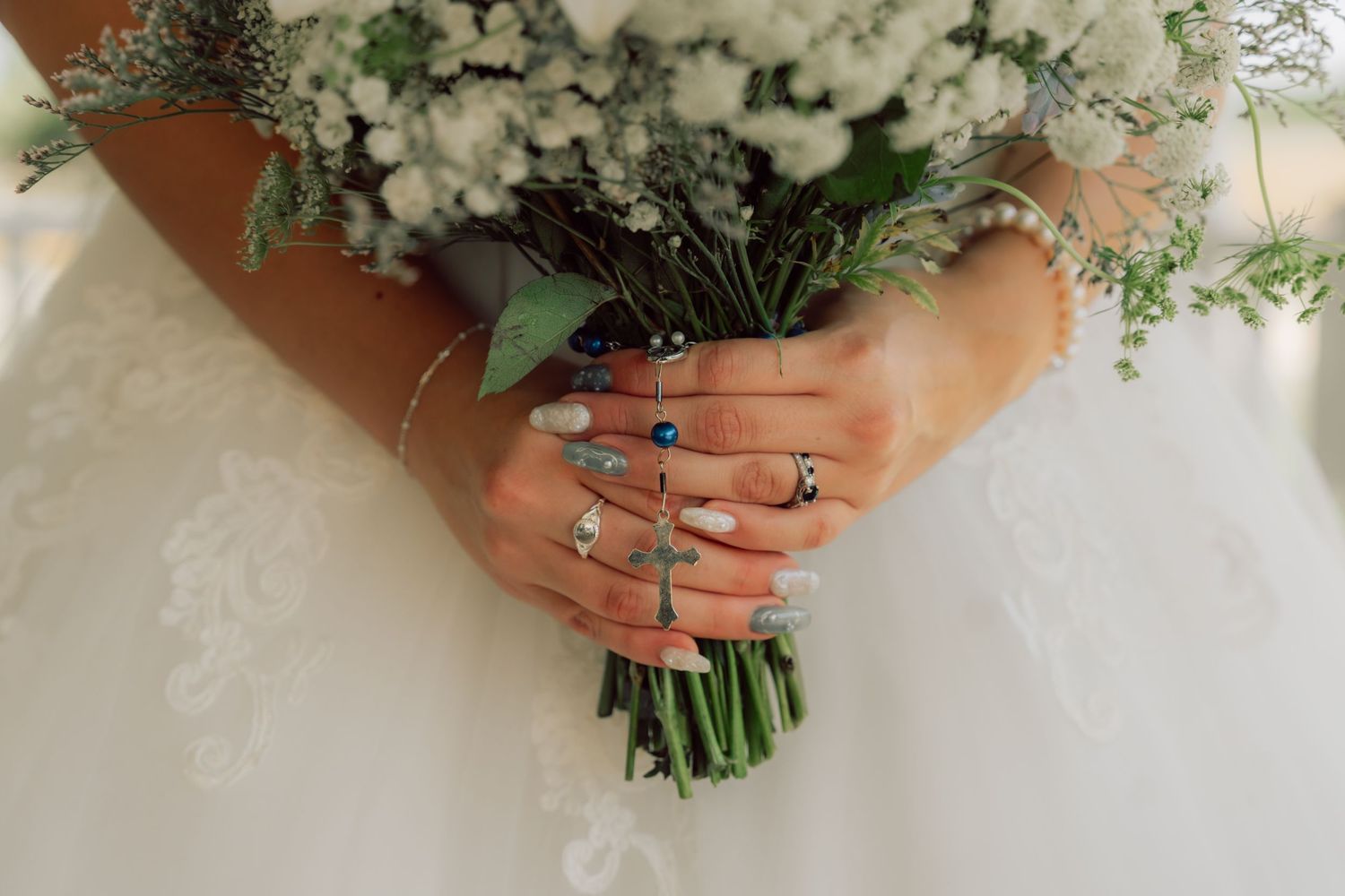 Close-up of hands holding a white and green wedding bouquet with baby's breath.