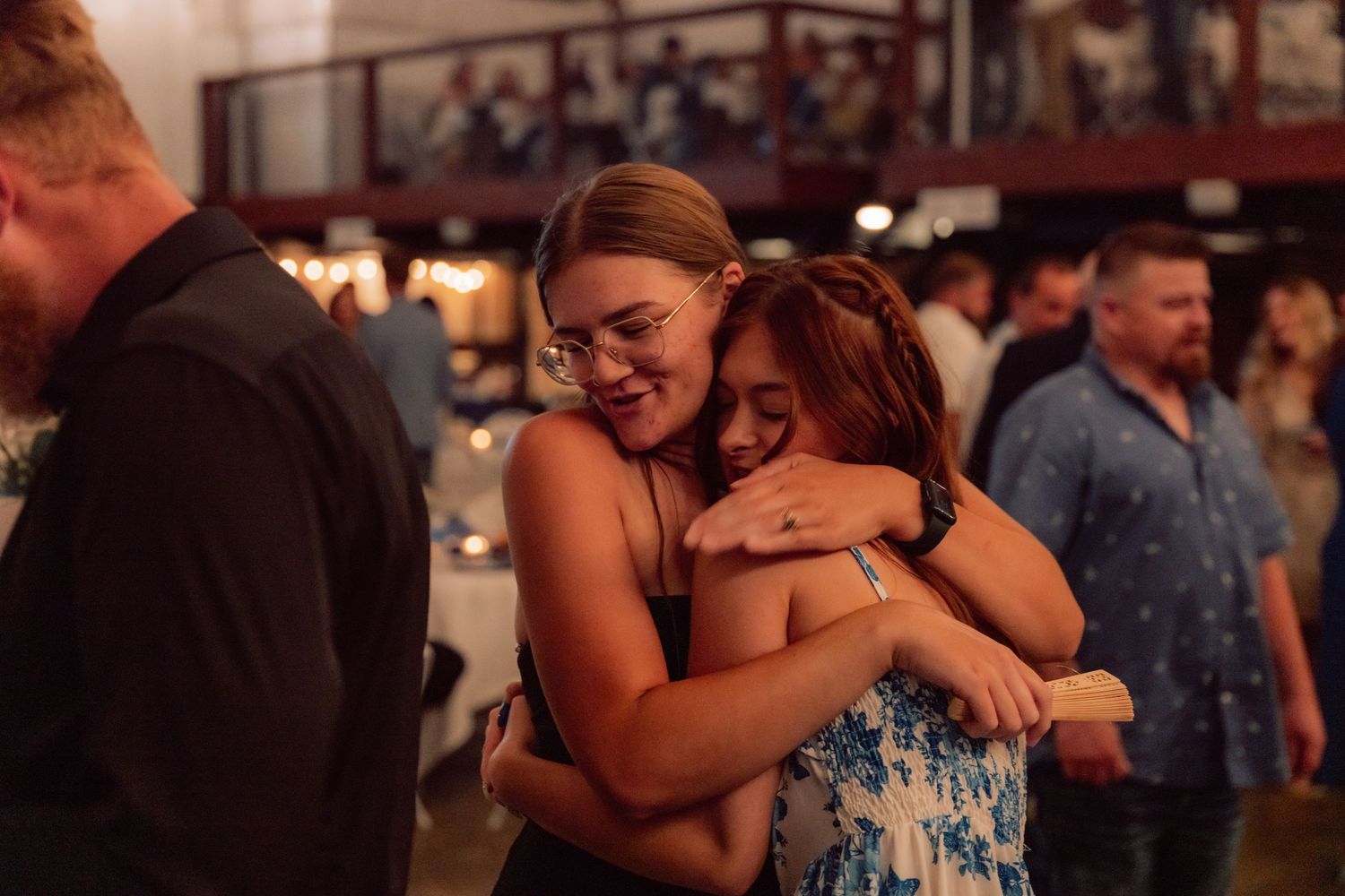 Guests sharing emotional embraces during a wedding reception in a rustic venue.