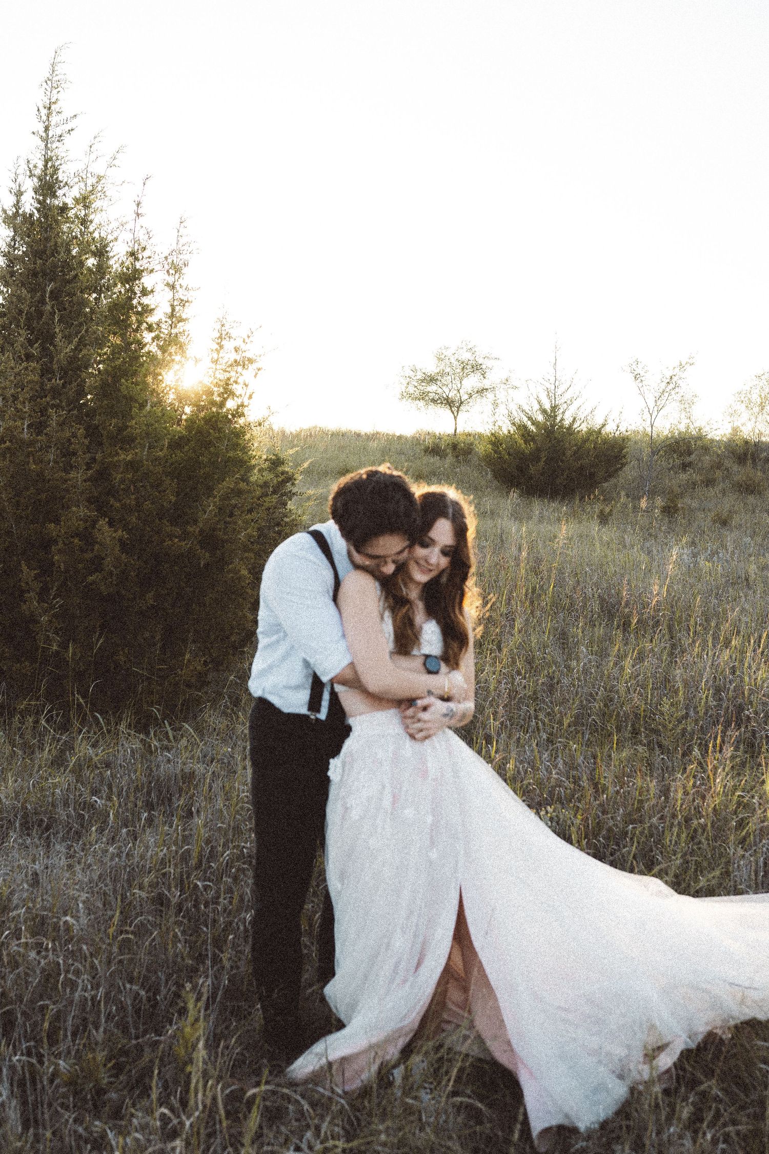 Newlywed couple shares an intimate moment in a golden field at sunset.