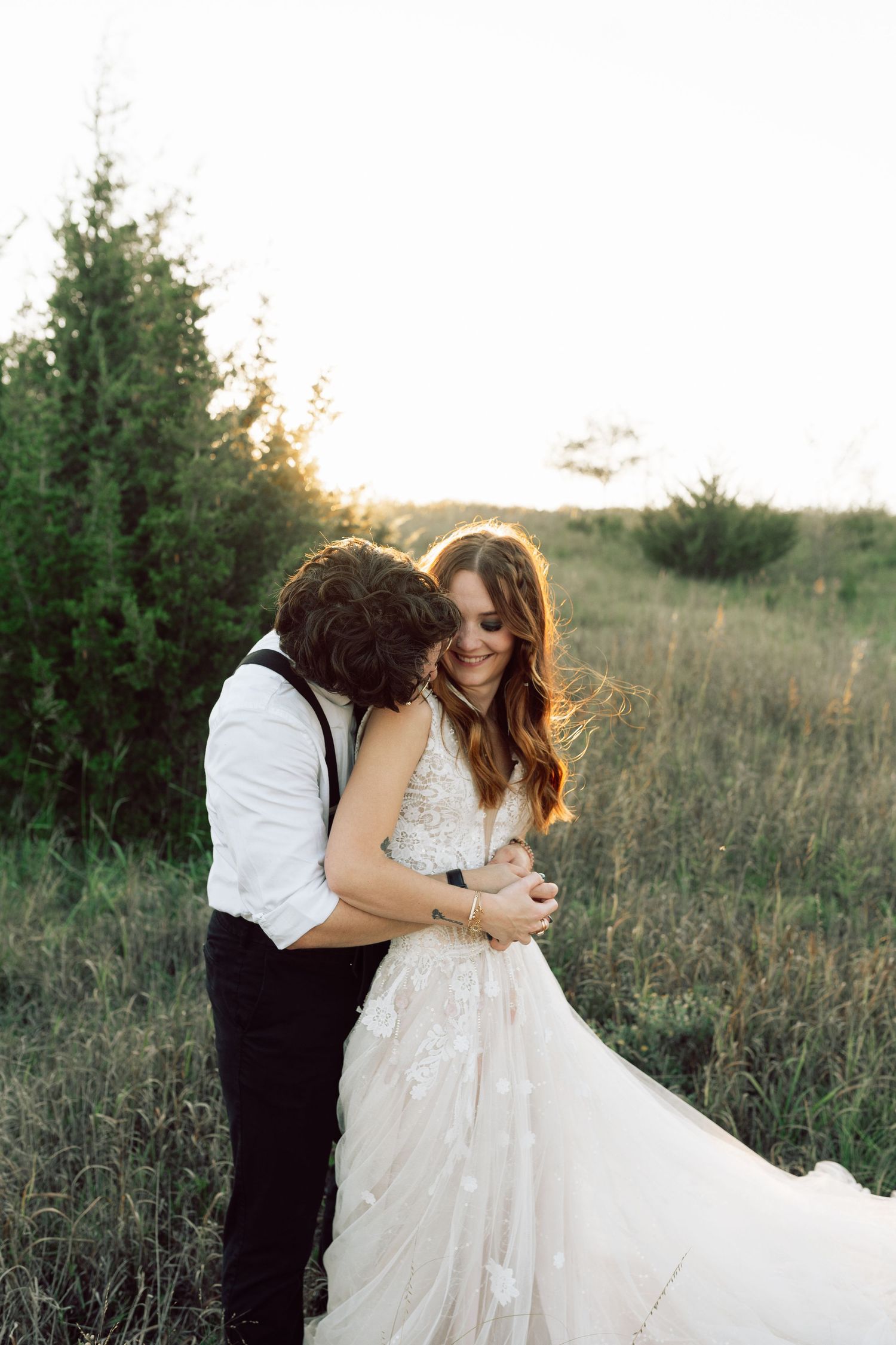 Wedding couple shares intimate moment in golden hour light among wild grasses.