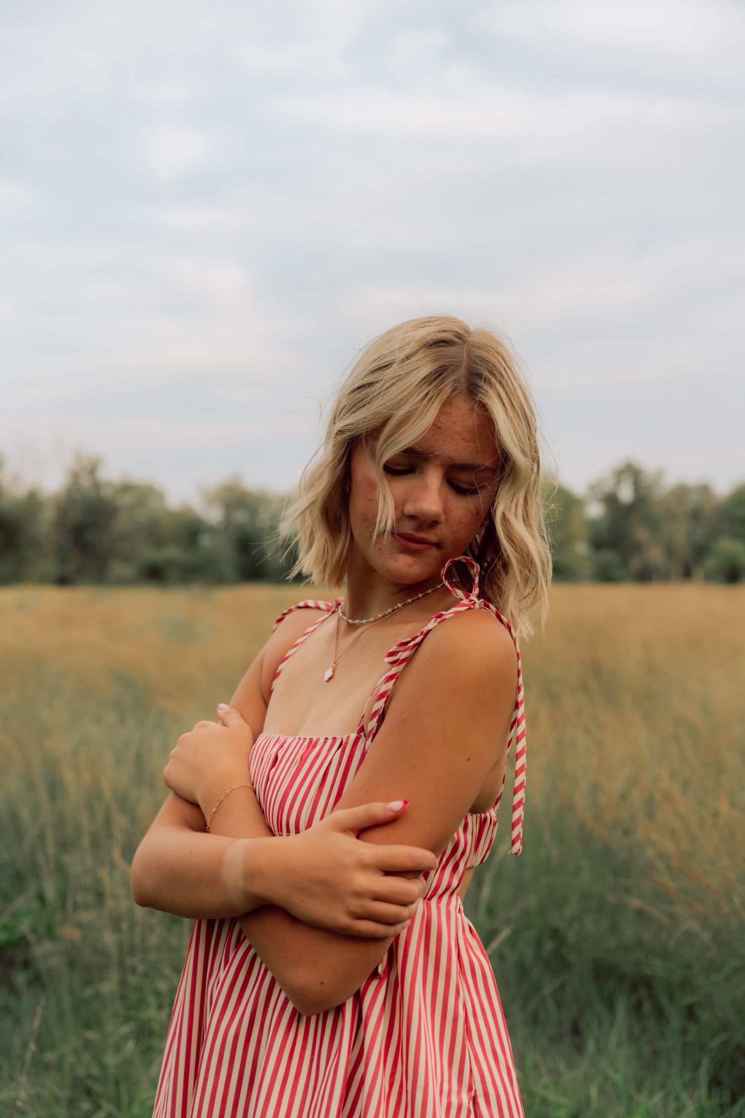 Person in red and white striped summer dress poses playfully in a grassy field during golden hour.