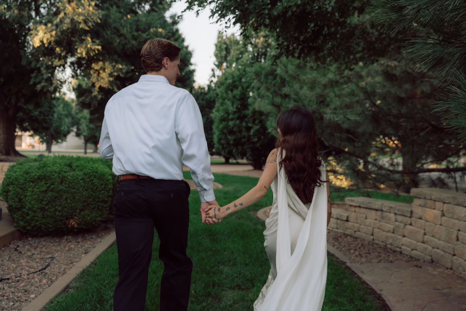 A couple holds hands while walking through a landscaped garden path at sunset.