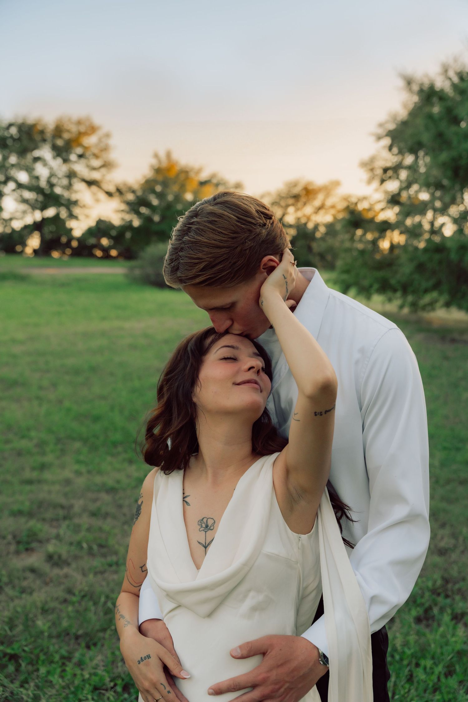 An intimate portrait of a couple embracing in white clothing against a natural outdoor setting.