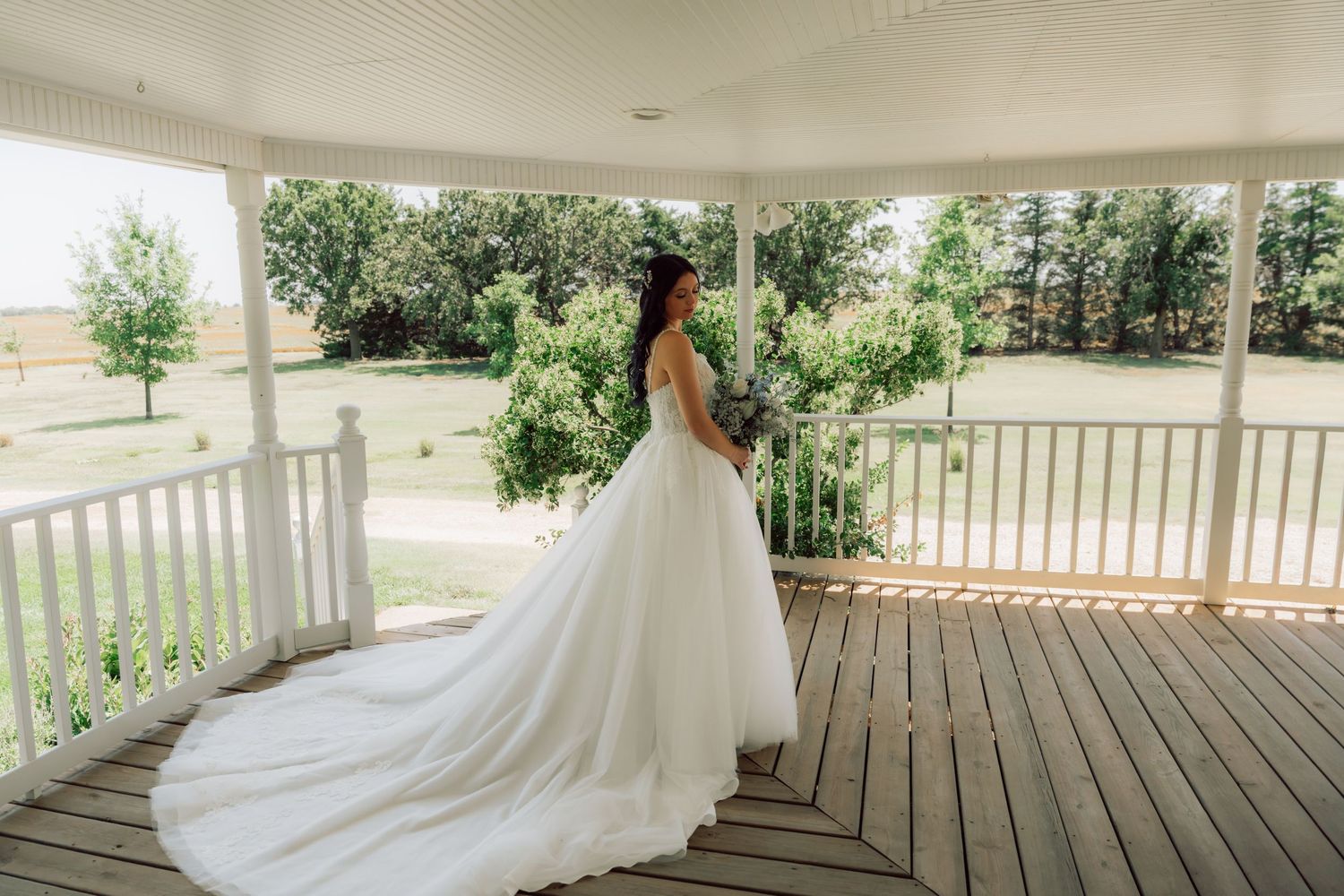 White wedding dress with full skirt trails across wooden porch boards in natural light.