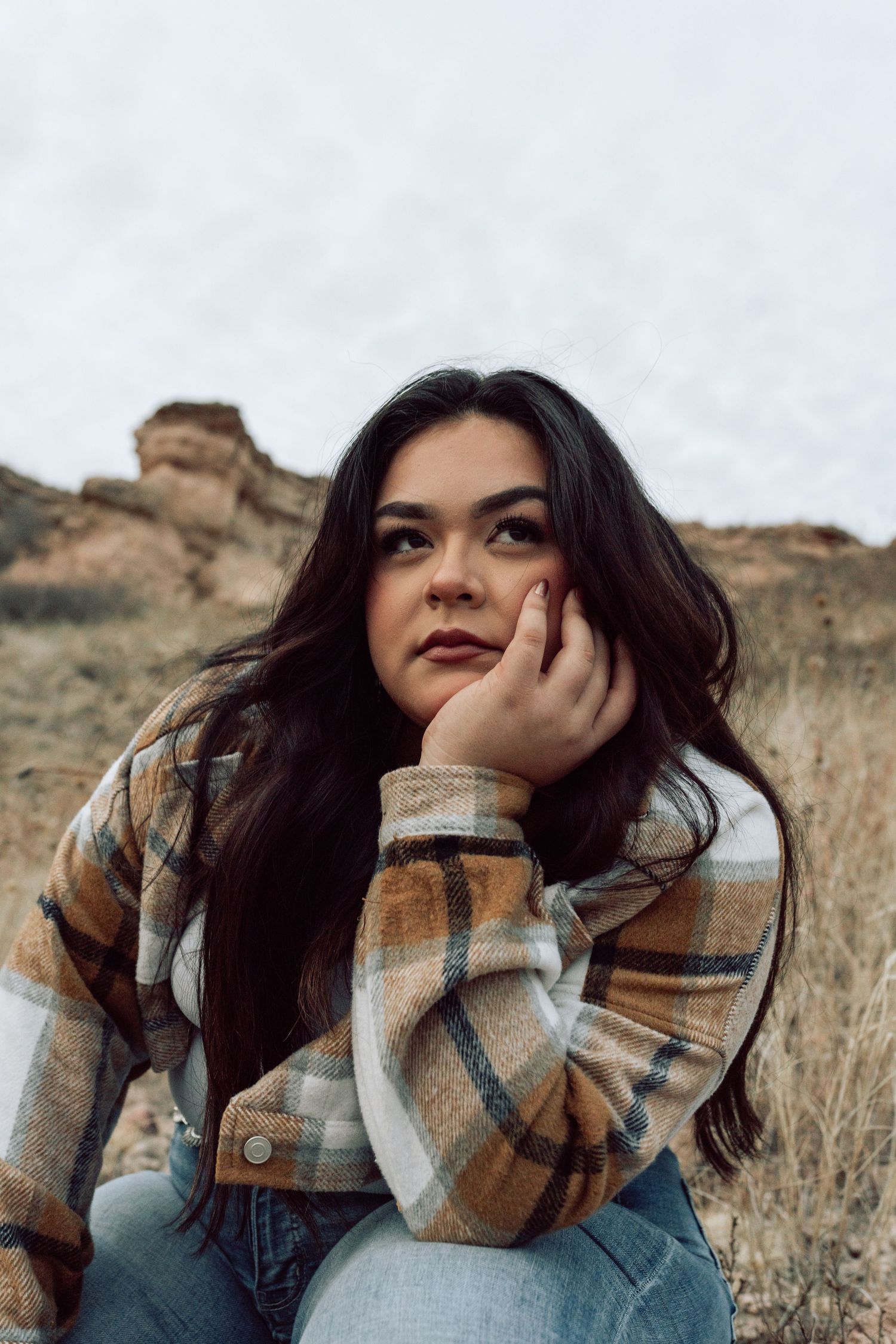 Person in plaid flannel poses thoughtfully in autumn field.