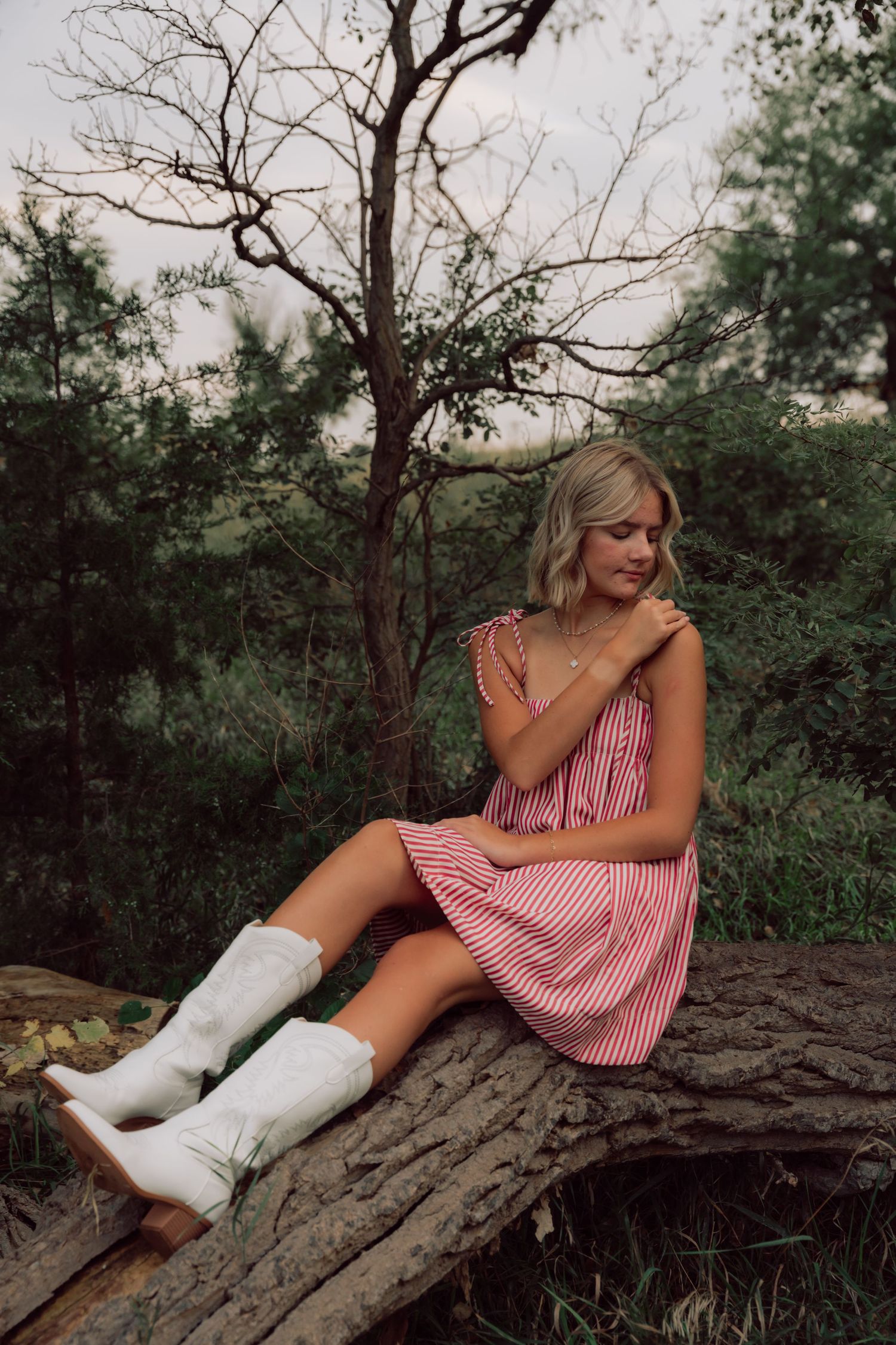 Person in striped dress and white boots poses on rocky surface near trees.