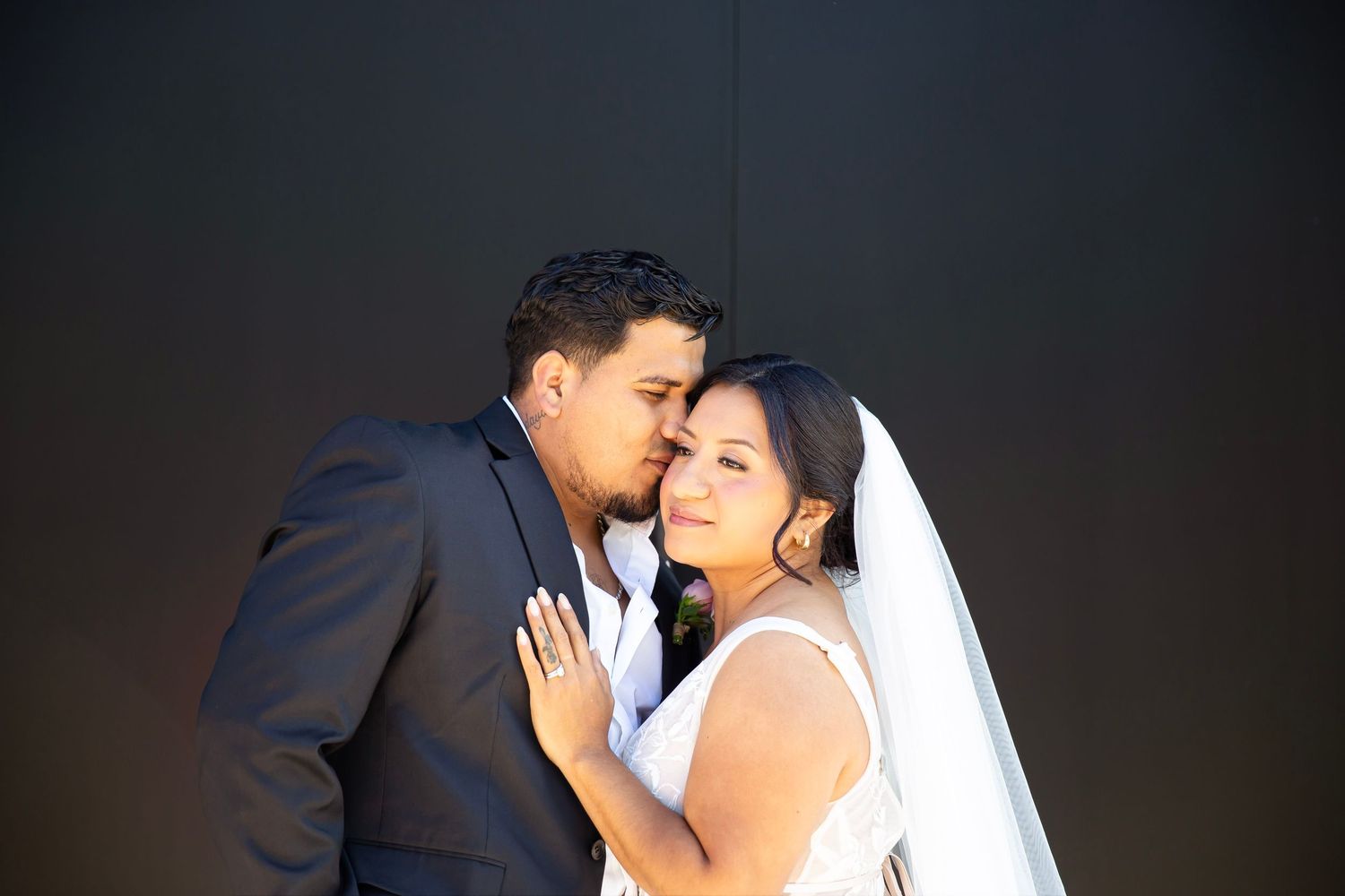 Bride leaning into groom's chest as he softly kisses her cheek.