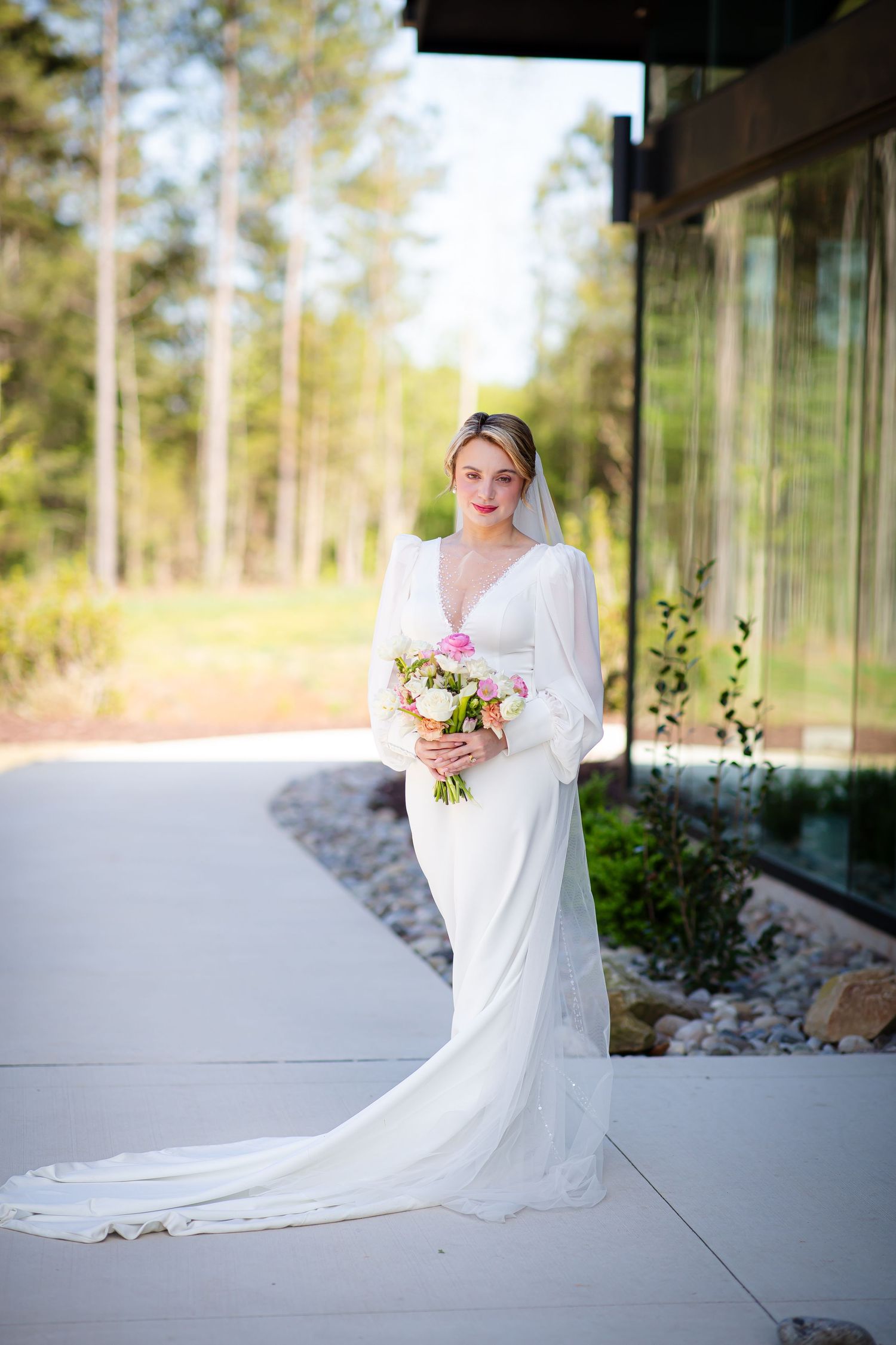 Bride in white dress holding a pink and white bouquet while her train surrounds her feet.