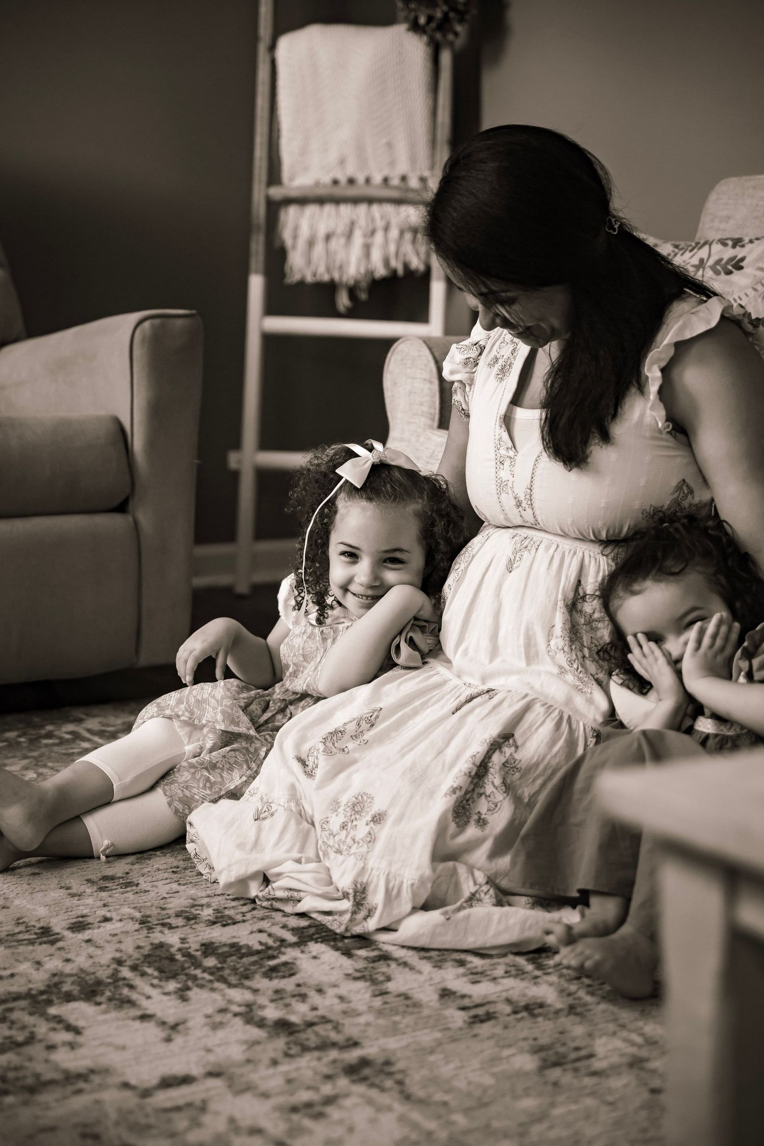 Mom holding two little girls on either side while sitting on the carpet