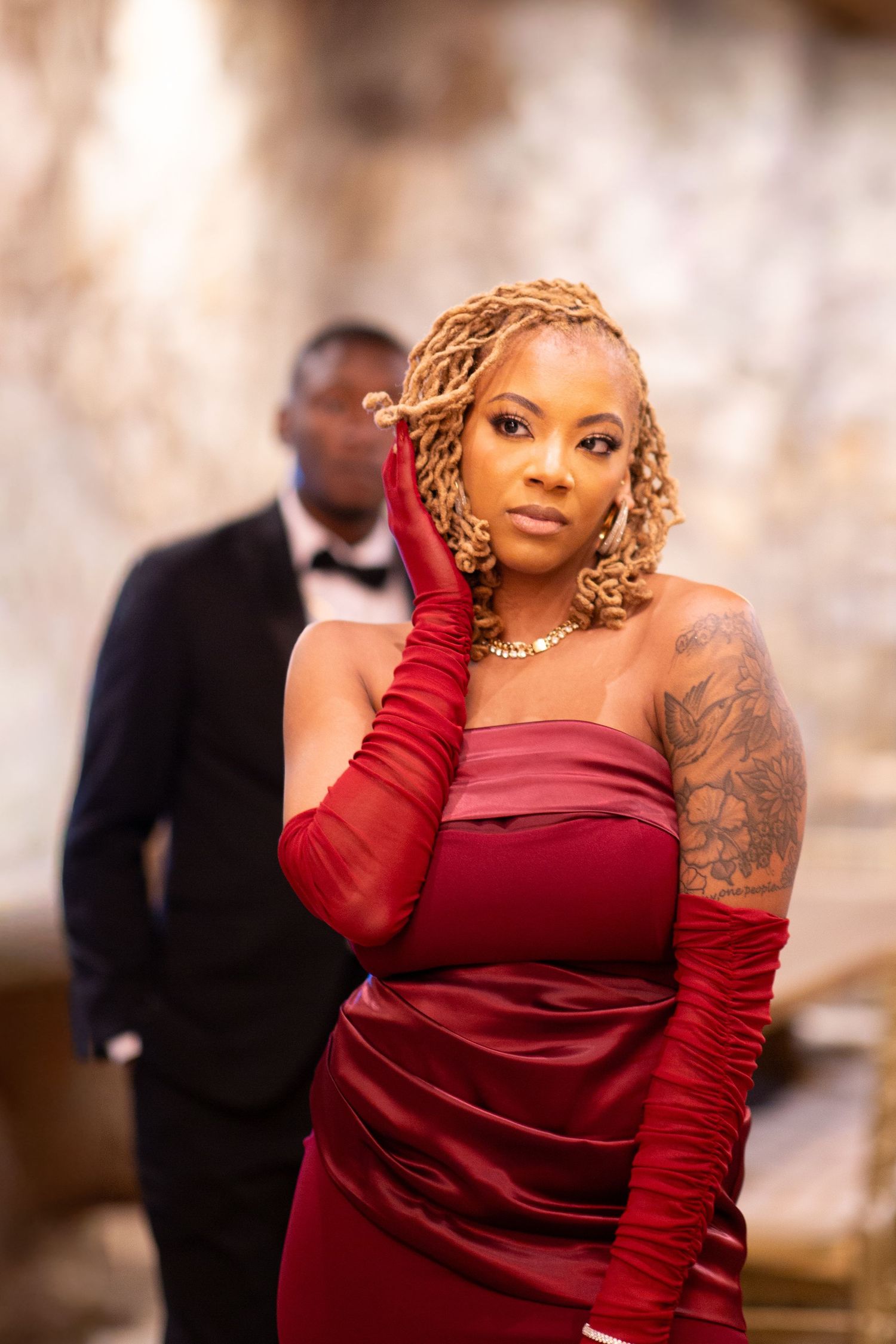 A Black woman in a red satin strapless gown with gloves poses elegantly indoors.