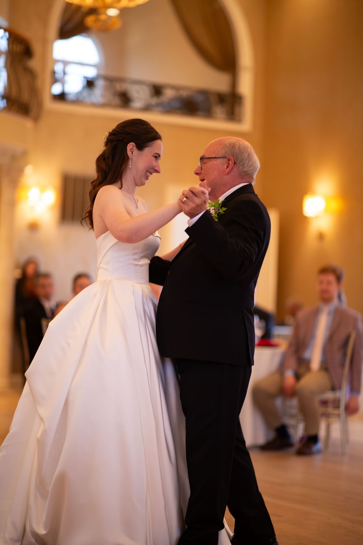 Bride in white ball gown sharing emotional father-daughter dance at warmly lit wedding reception.