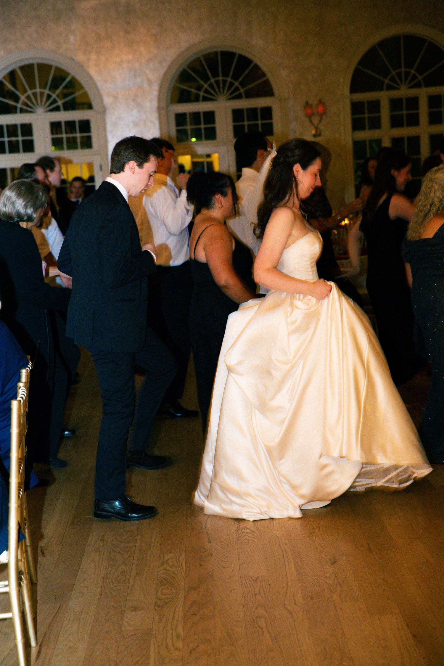 Wedding couple sharing a lively dance on the hardwood floor at a formal indoor reception.
