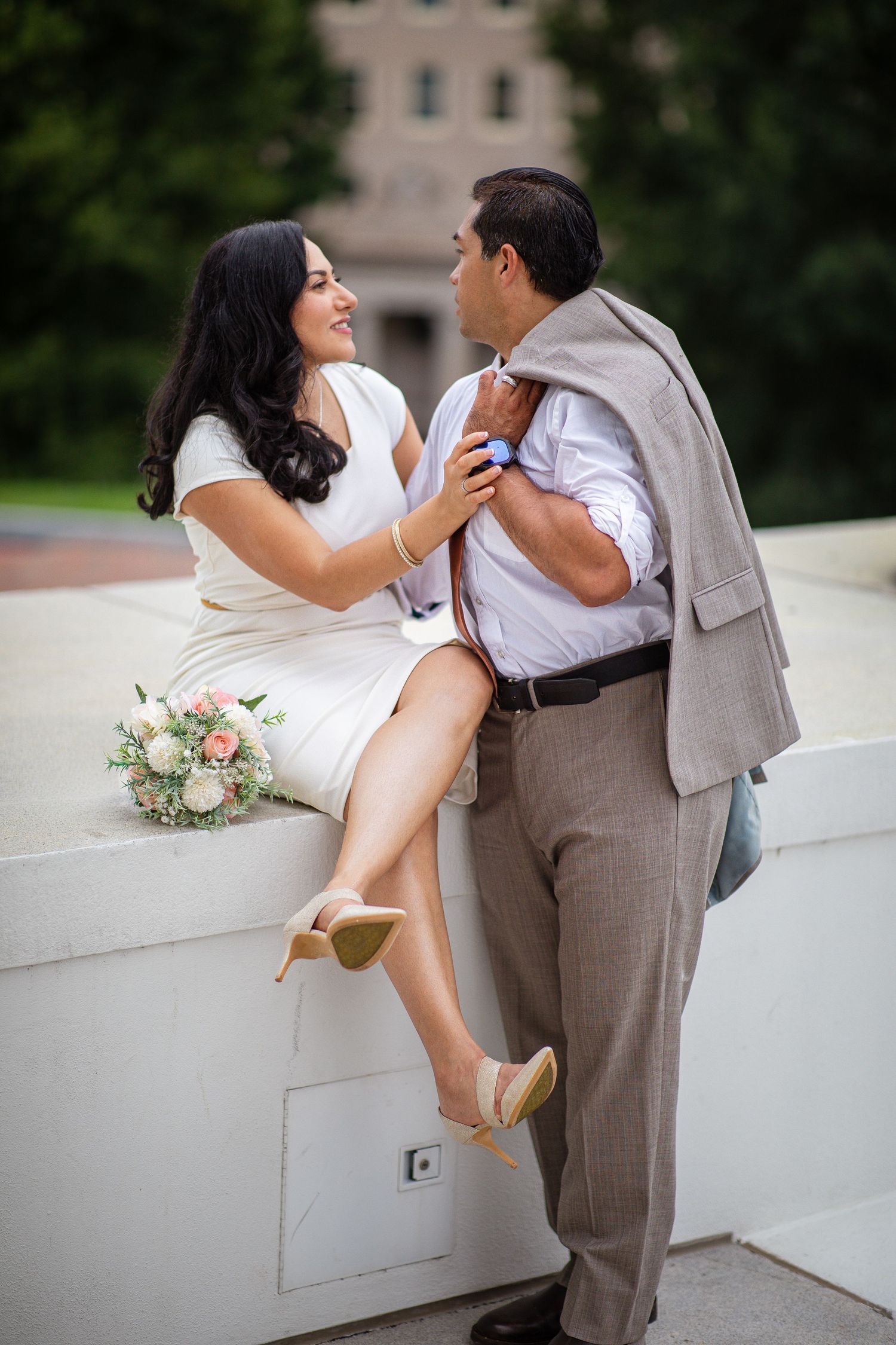 Couple in wedding attire sharing a romantic moment outdoors, woman in white dress with bouquet, man in gray suit.