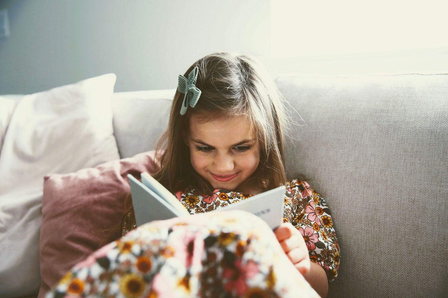 Young daughter reading book on couch.