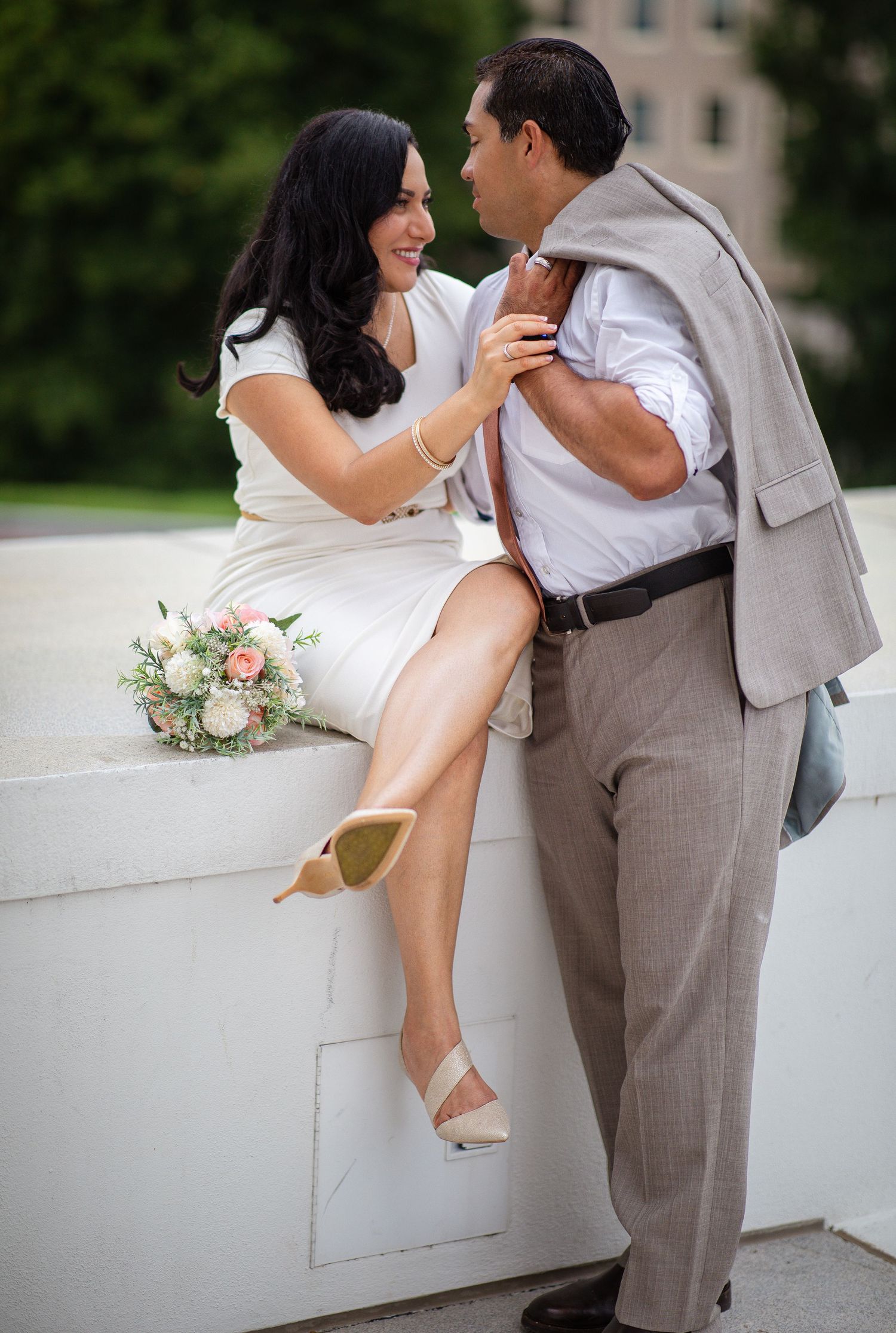 Couple in wedding attire sharing a romantic moment outdoors, bride in white dress holding bouquet, groom in tan suit.