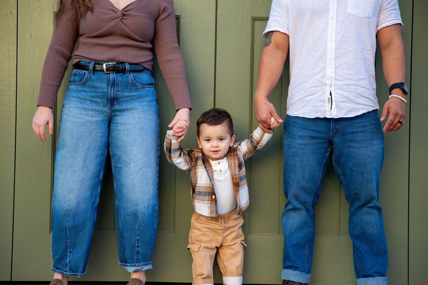 Mother and father holding  the hands of their baby boy standing between them