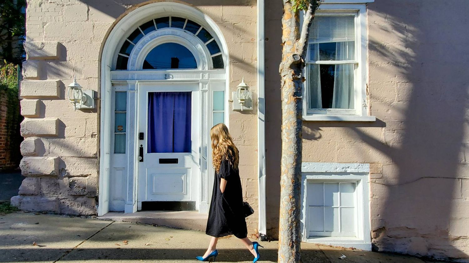 Young lady walking along a sidewalk in front of a building.