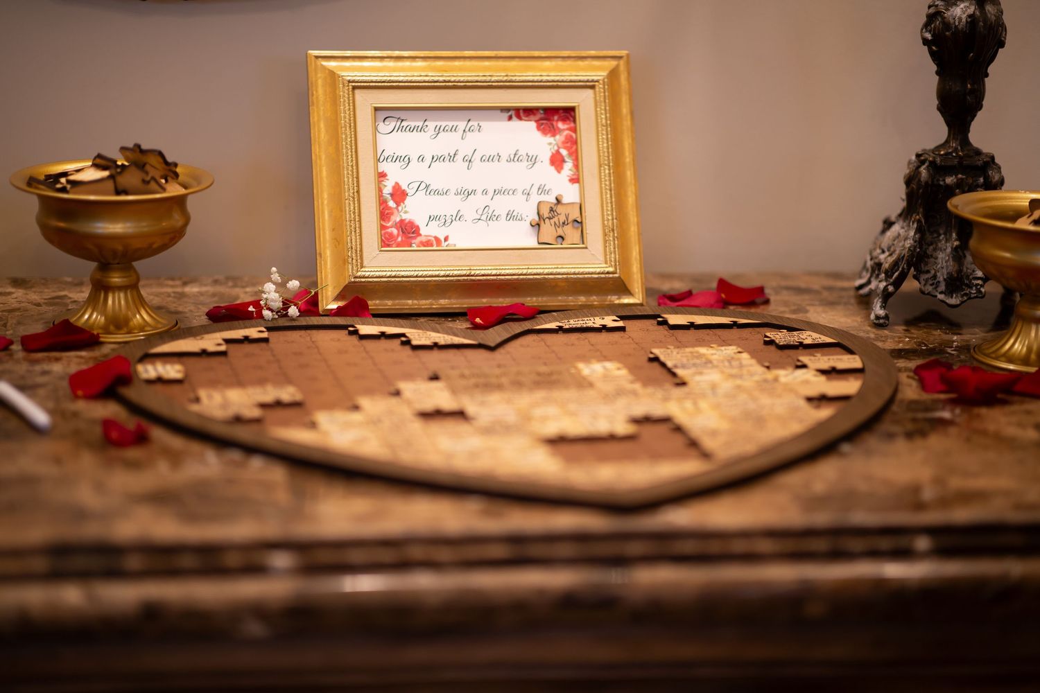 Wooden heart-shaped wedding guest puzzle book with framed sign and rose petals on rustic table.