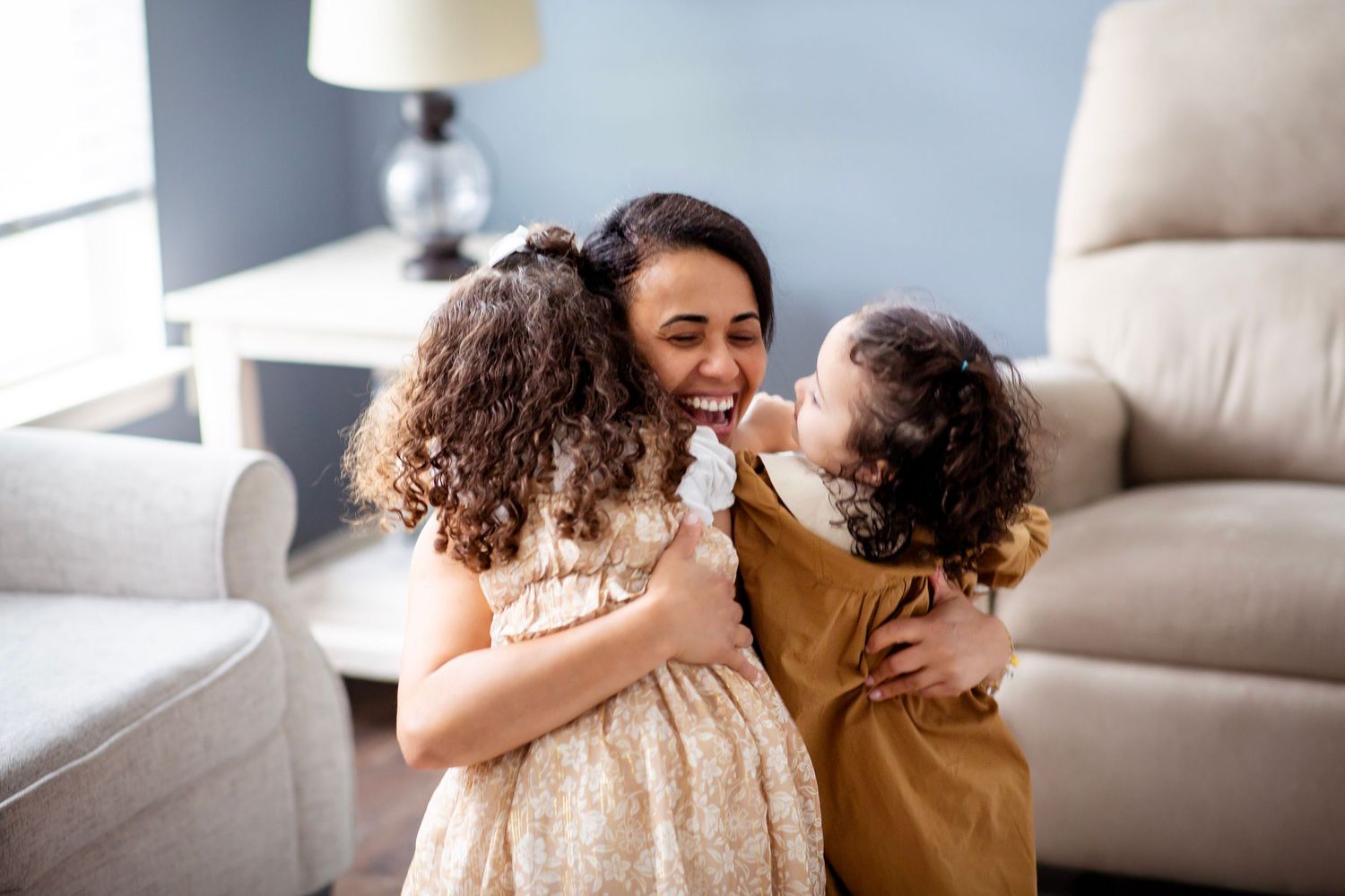 Mom embracing her two little girls from a kneeling position