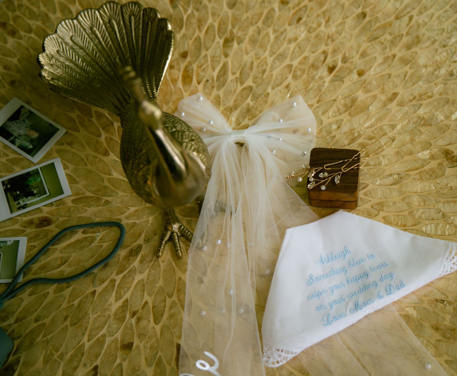 Wedding flat lay featuring a bronze bird statue, bridal veil, jewelry box, and handwritten handkerchief on stone.