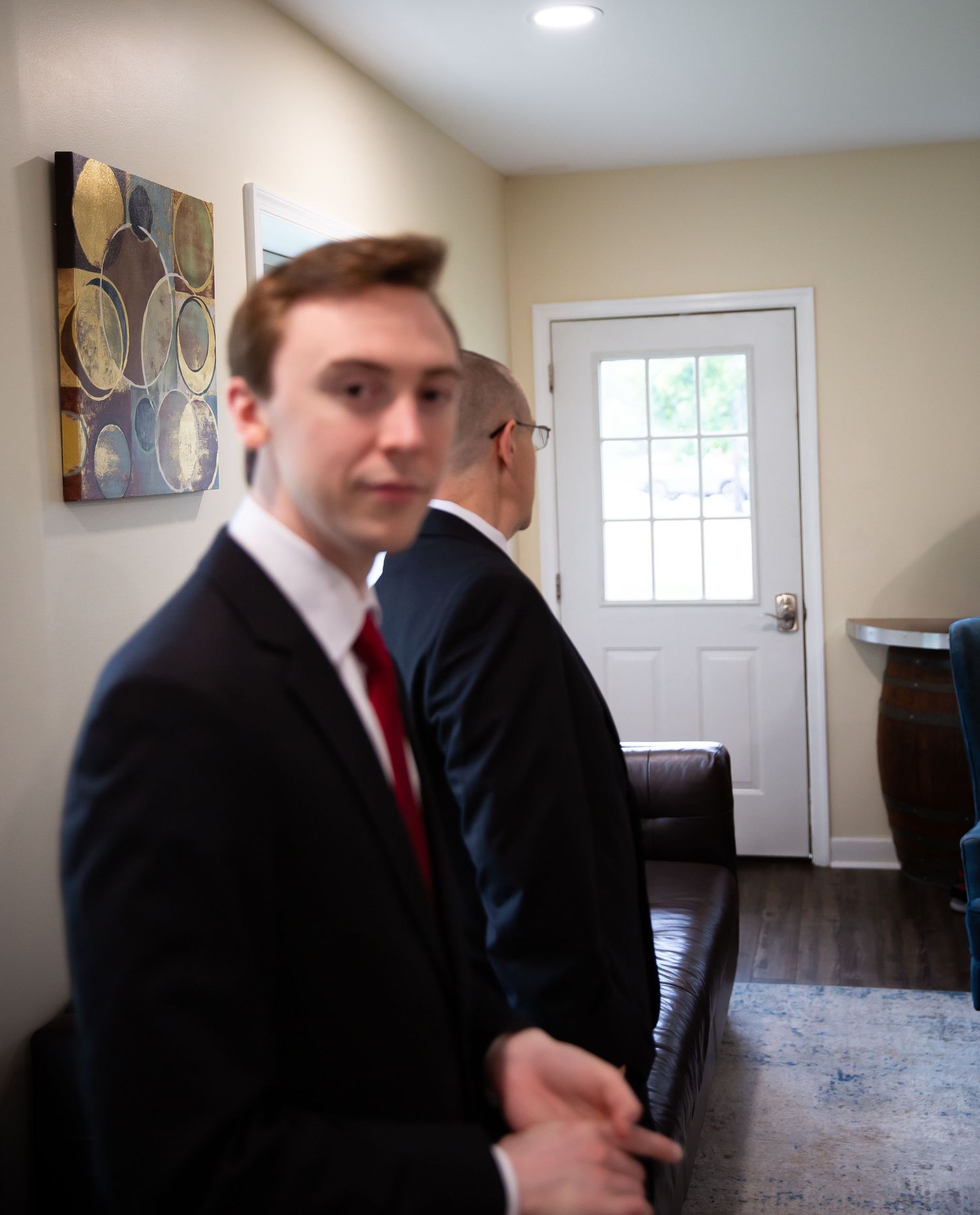 Two men in black suits with red ties standing in home entryway before wedding.