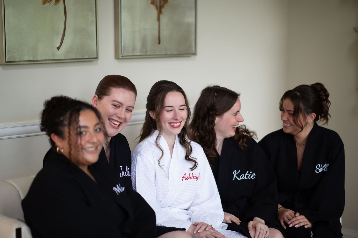 Bride and bridesmaids laughing together wearing personalized black and white robes.
