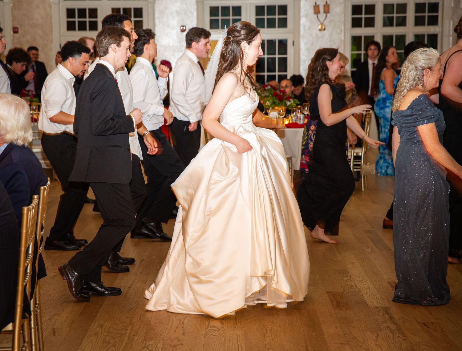 Bride in ivory ball gown dances joyfully with guests at wedding reception.