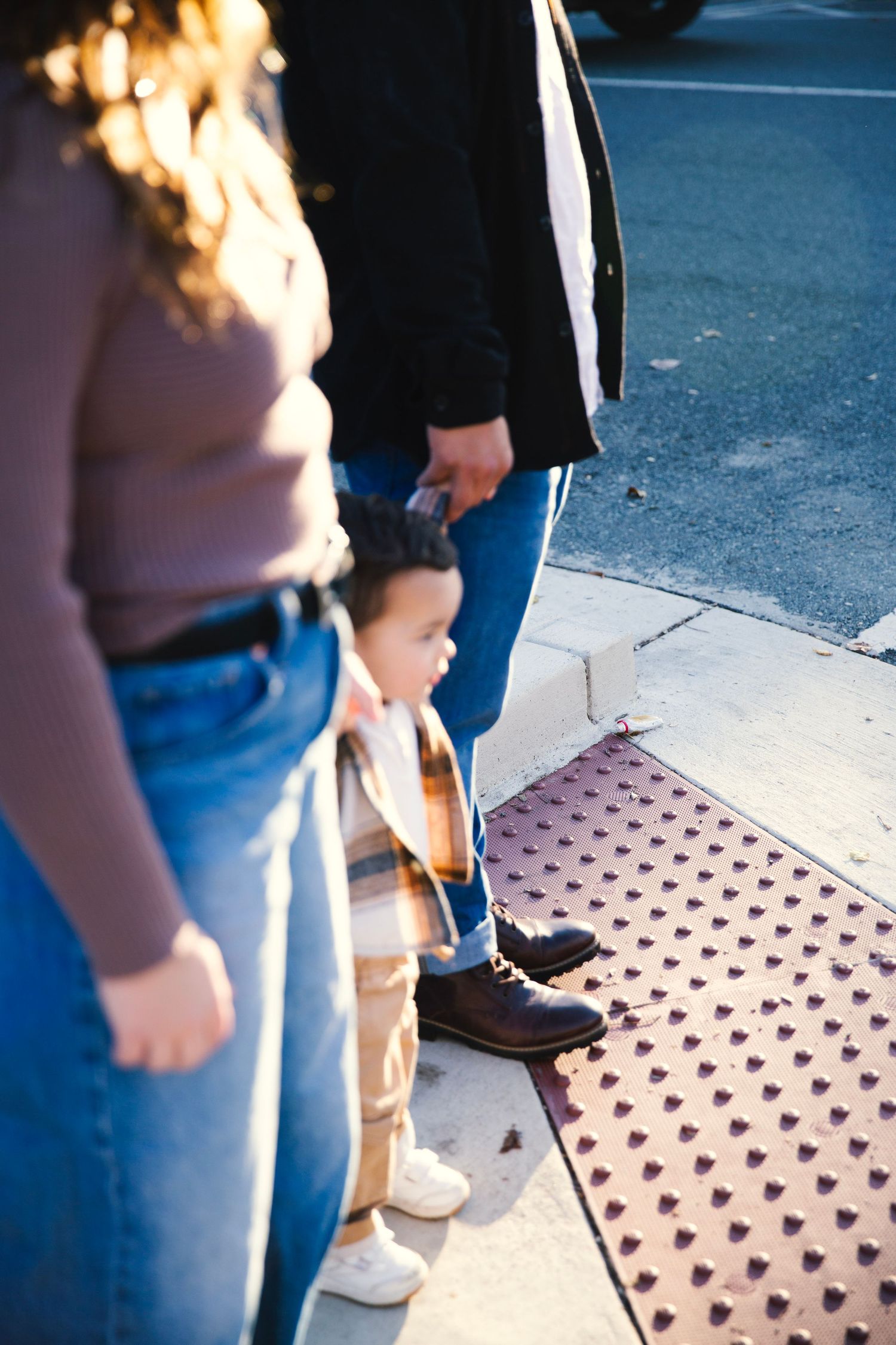 Mother and father holding  the hands of their baby boy standing between them in golden hour