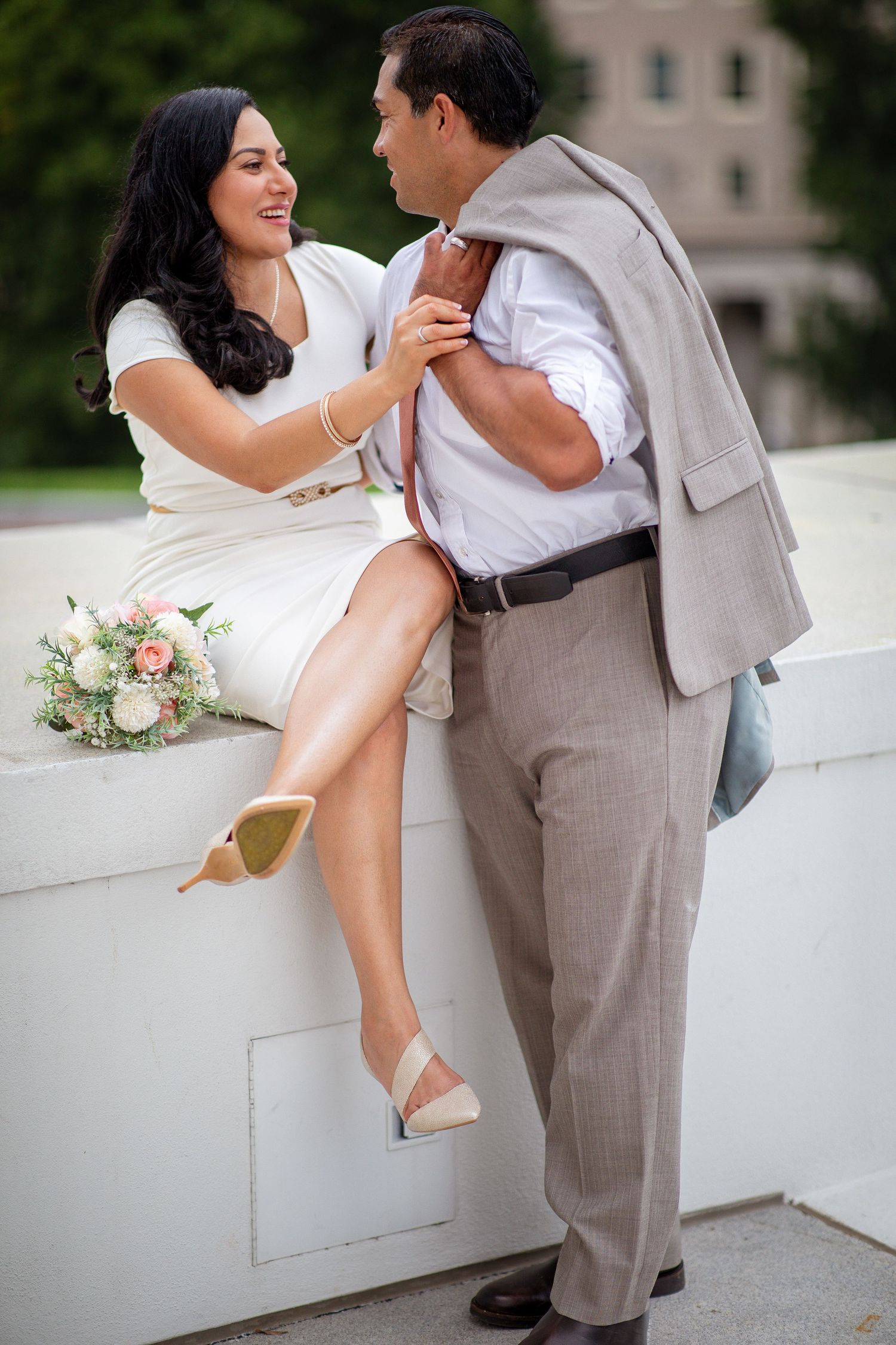Couple in wedding attire sharing a romantic moment, bride in white dress holding bouquet, groom in gray suit outdoors.