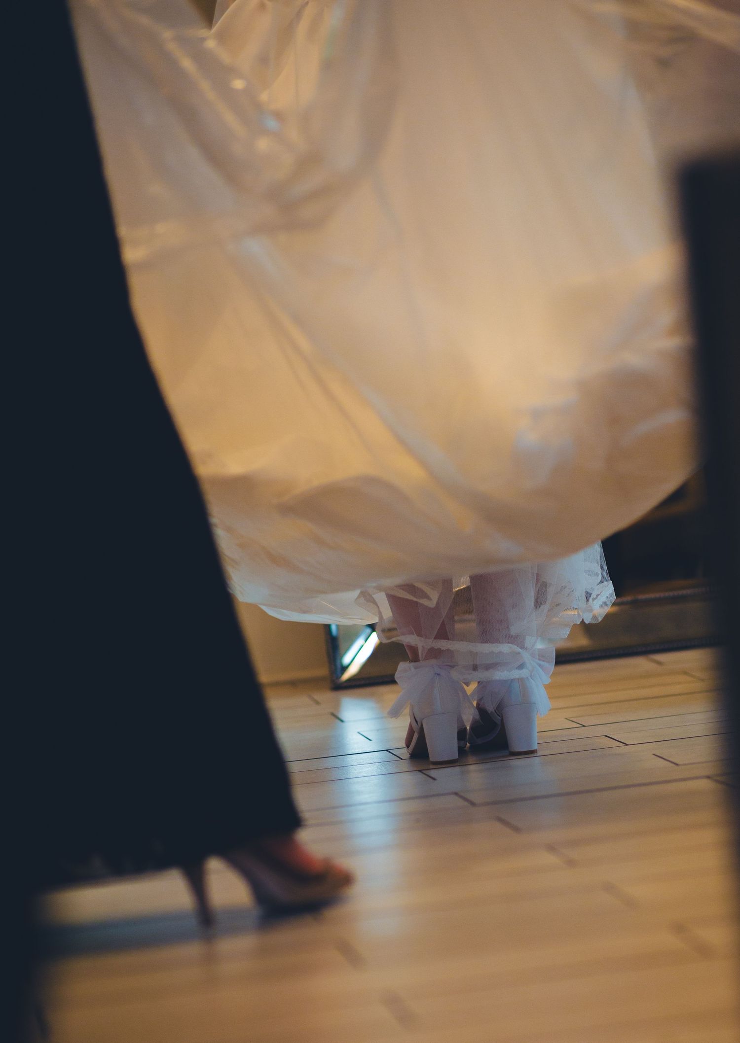 Close-up of bride's white wedding gown and shoes on wooden floor heading to the ceremony.