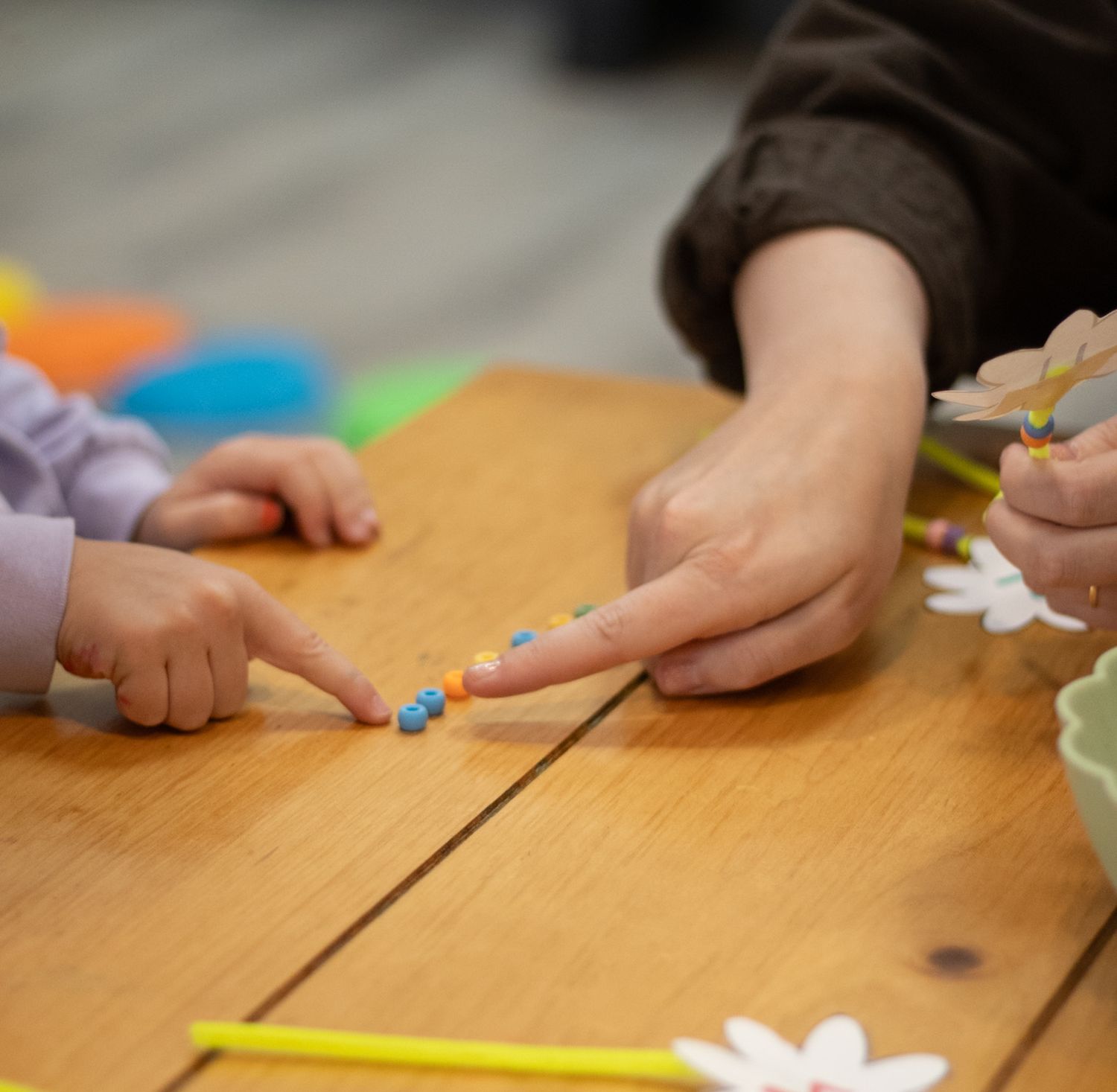 Adult and child hands playing with colorful beads on a wooden table during a creative learning activity.