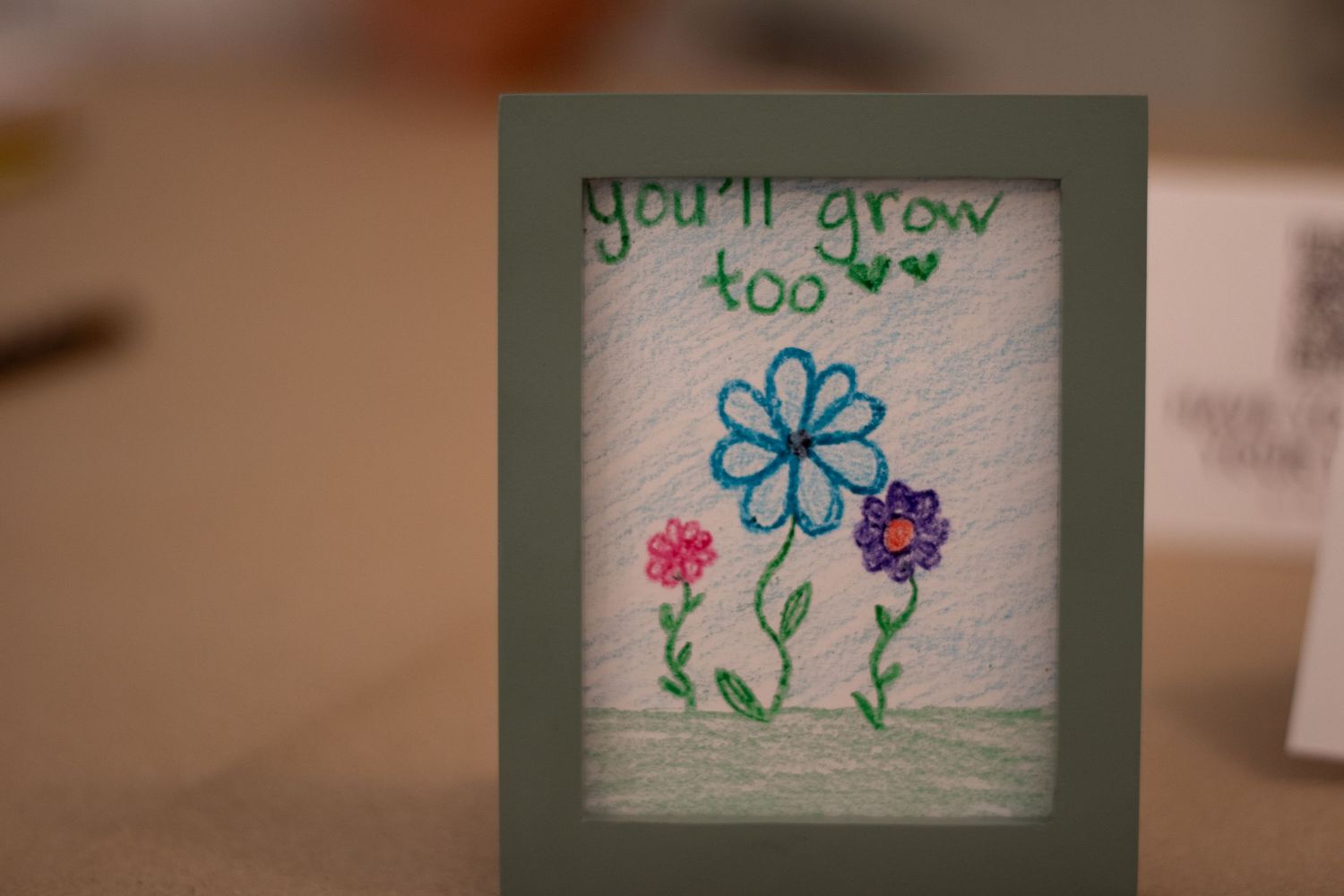 Handmade greeting card with embroidered flowers and text reading you'll grow too in a green frame.
