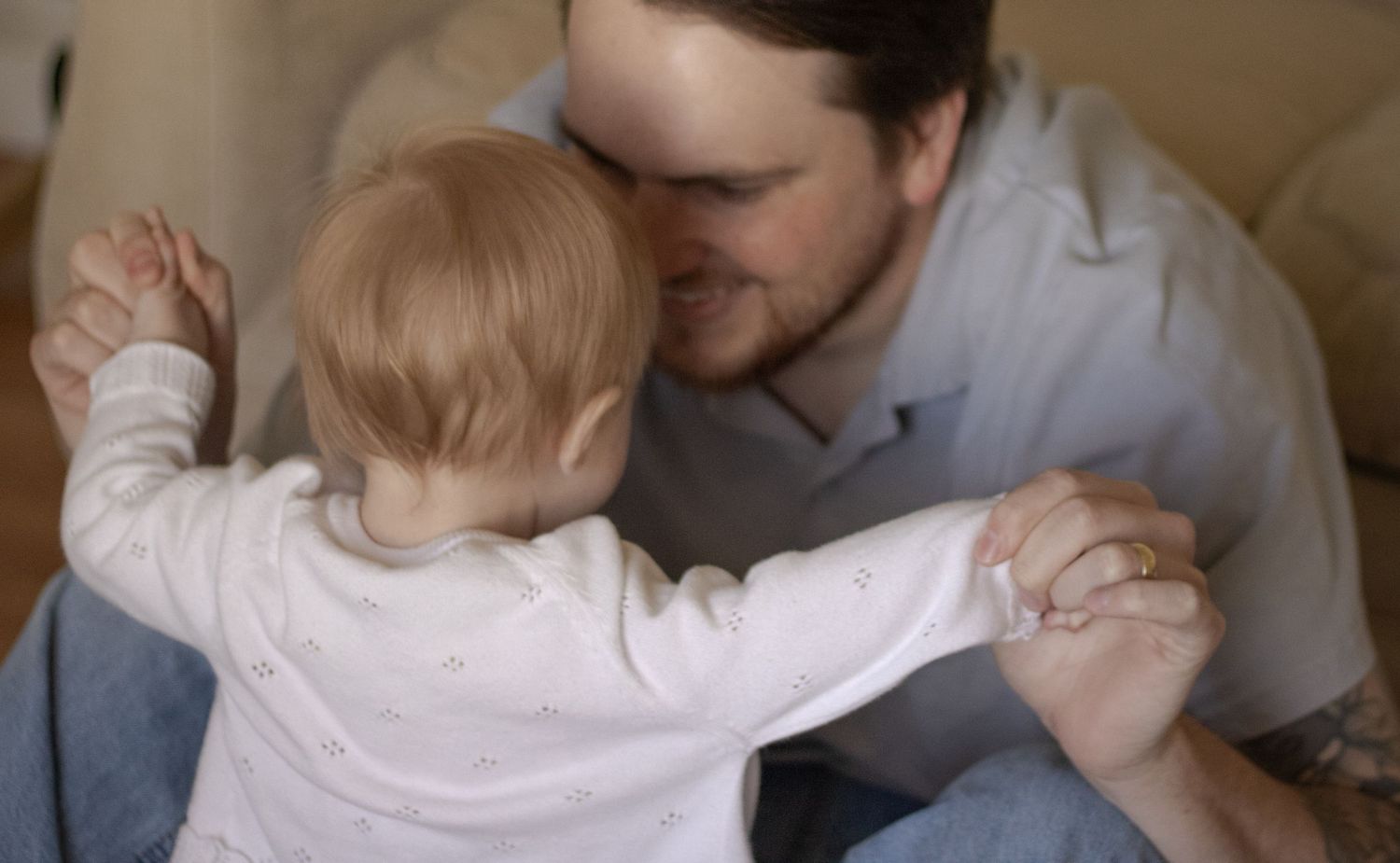 A father holds his baby's hands as the infant stands on his lap, sharing a tender bonding moment.