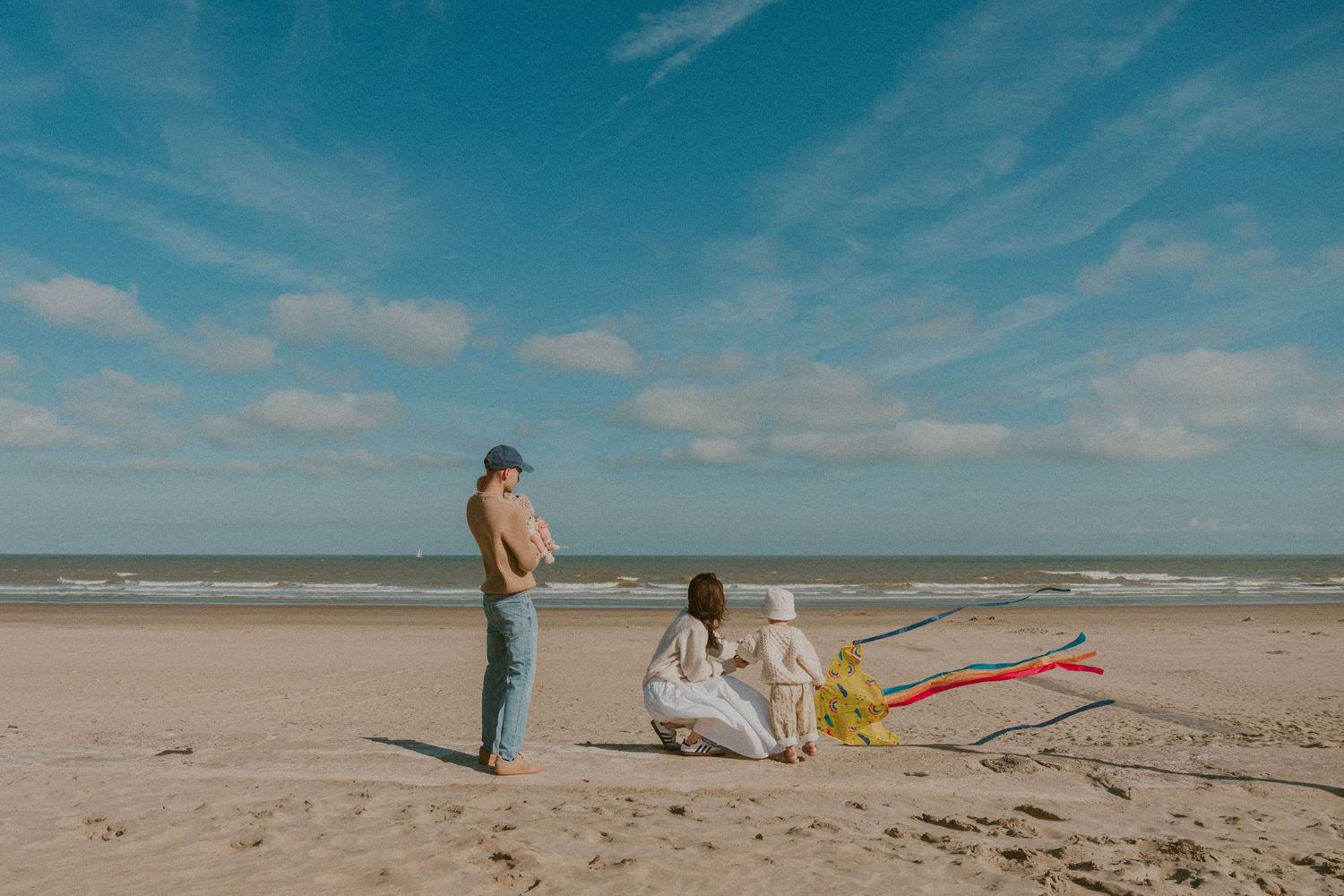 Family sitting on a sunny beach with a colorful kite on a bright day.