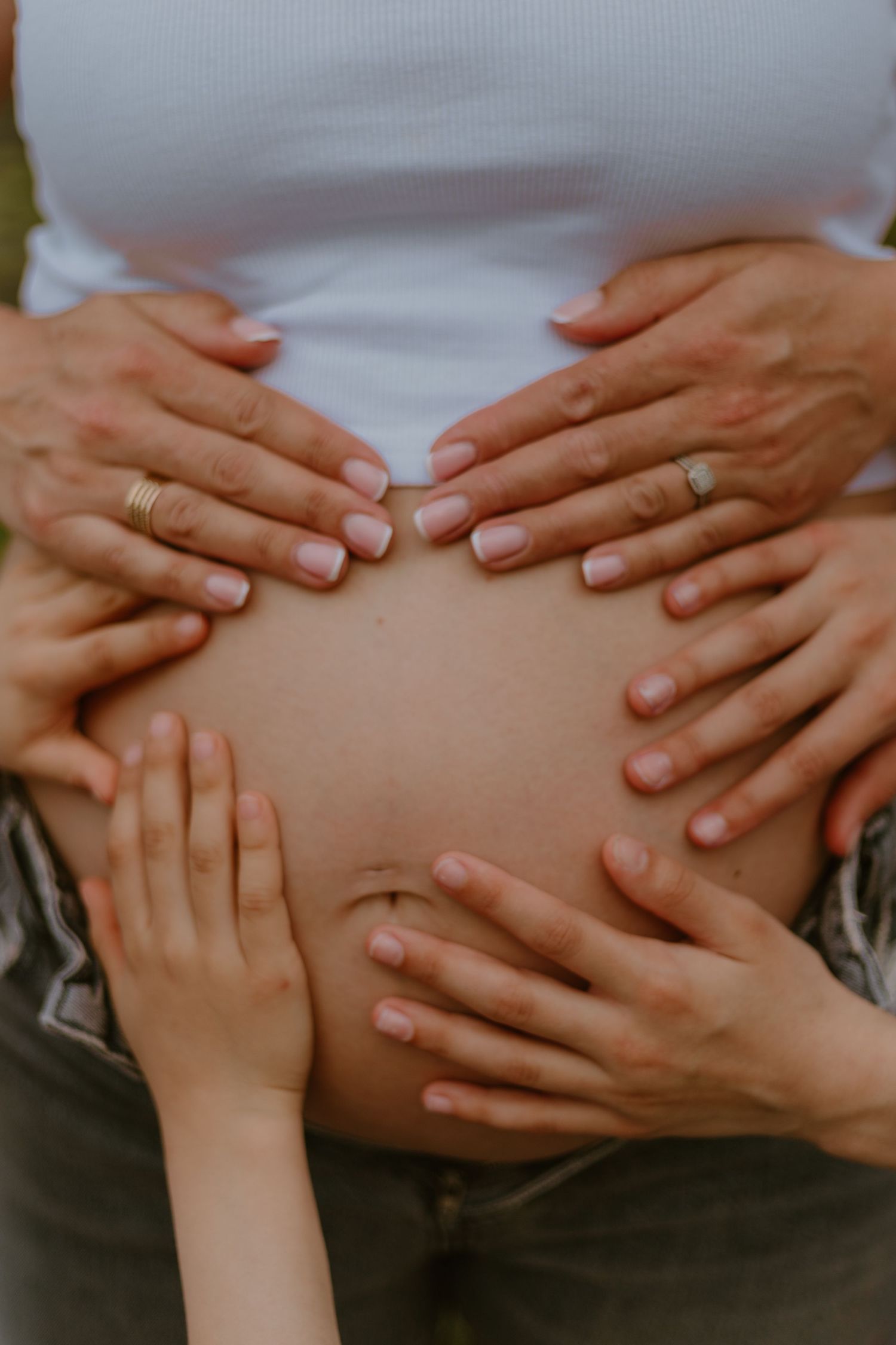 Multiple hands lovingly cradling a pregnant belly, including small child hands at the bottom.