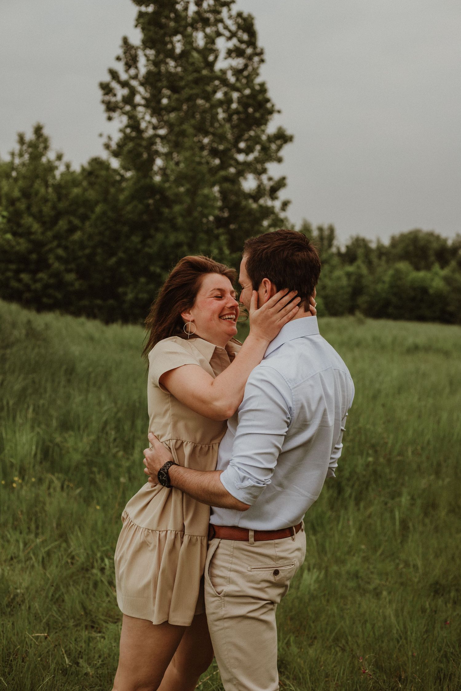 Happy couple embracing and smiling in a lush green meadow on an overcast day.