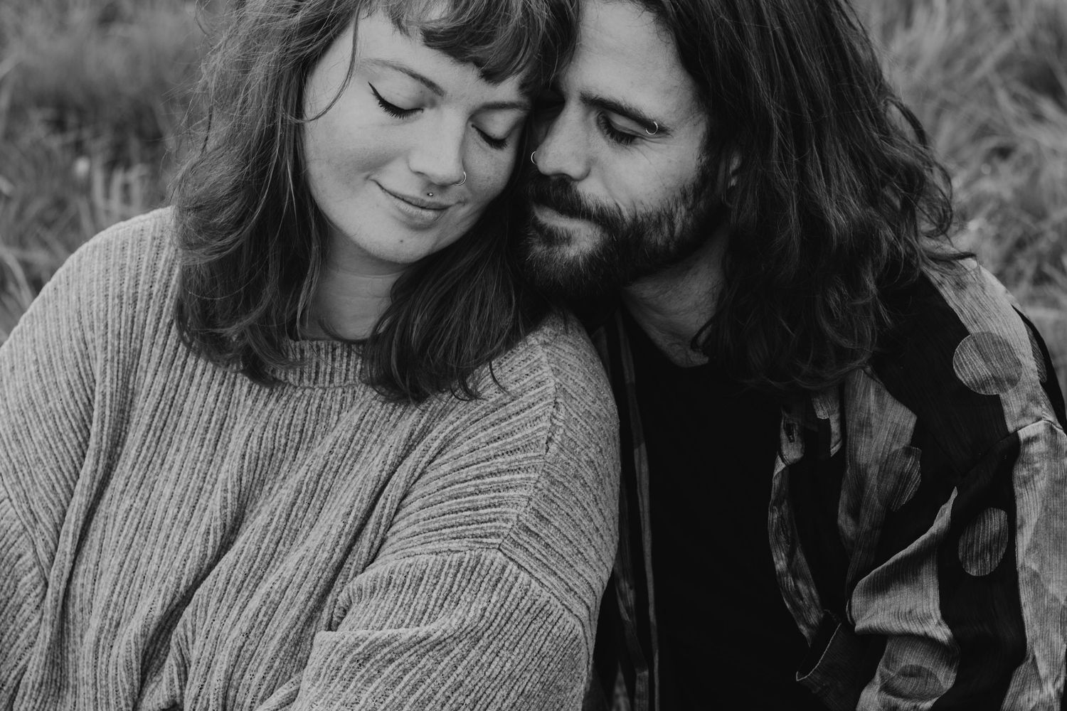 Black and white portrait of a couple snuggling closely together outdoors.